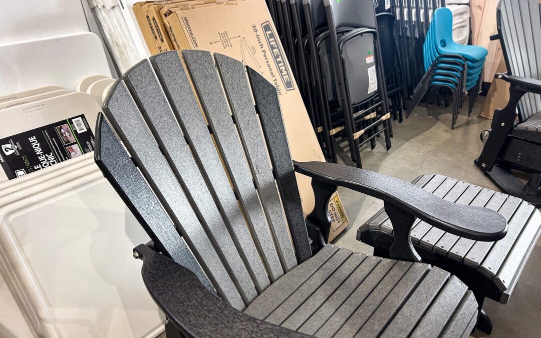 Shetler's Supplies Hardware Variety Bulk Foods Greenville PA A gray Adirondack chair is displayed in a store aisle alongside stacked folding chairs, tables, and boxed items.