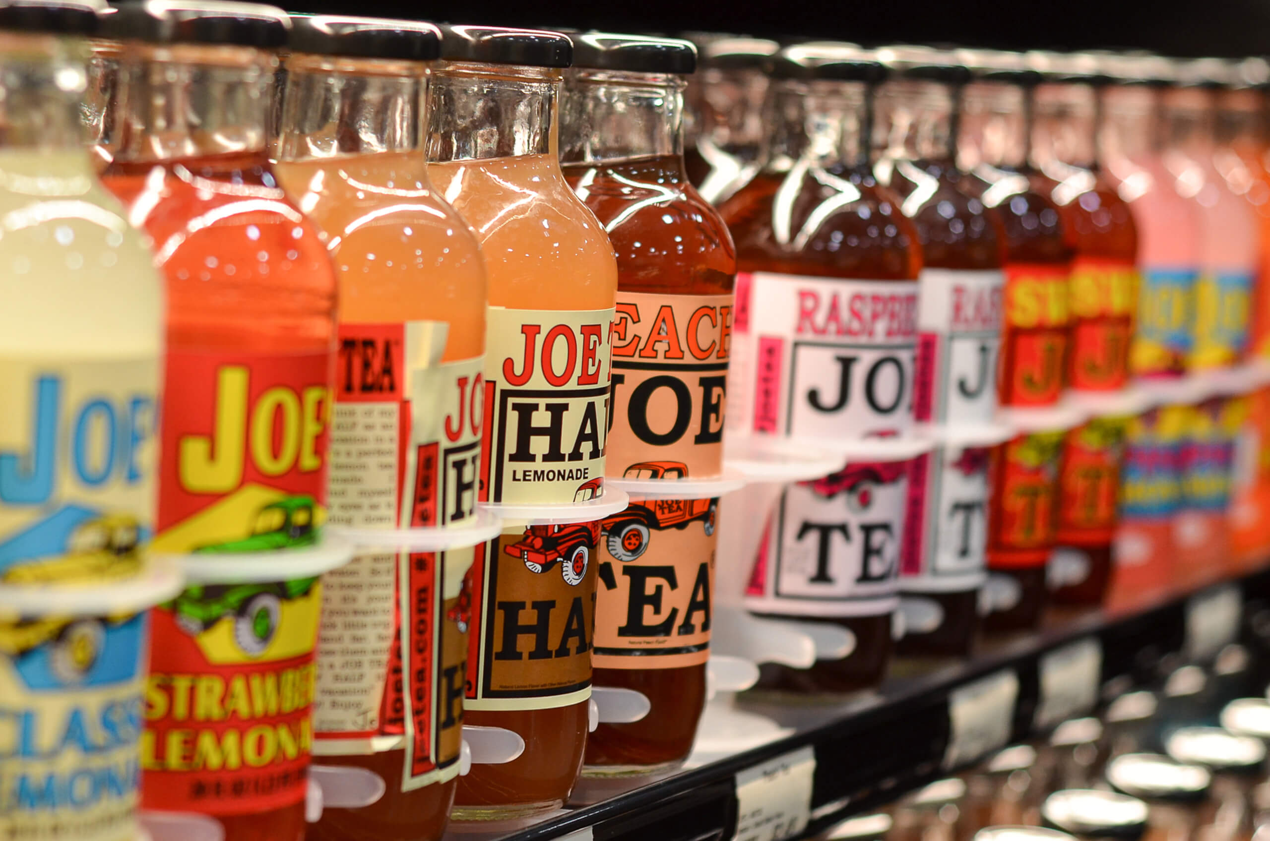Nolt's Country Market Eldon, Missouri Multiple glass bottles of Joe Tea and Joe Lemonade with colorful labels are displayed in a row on a store shelf.