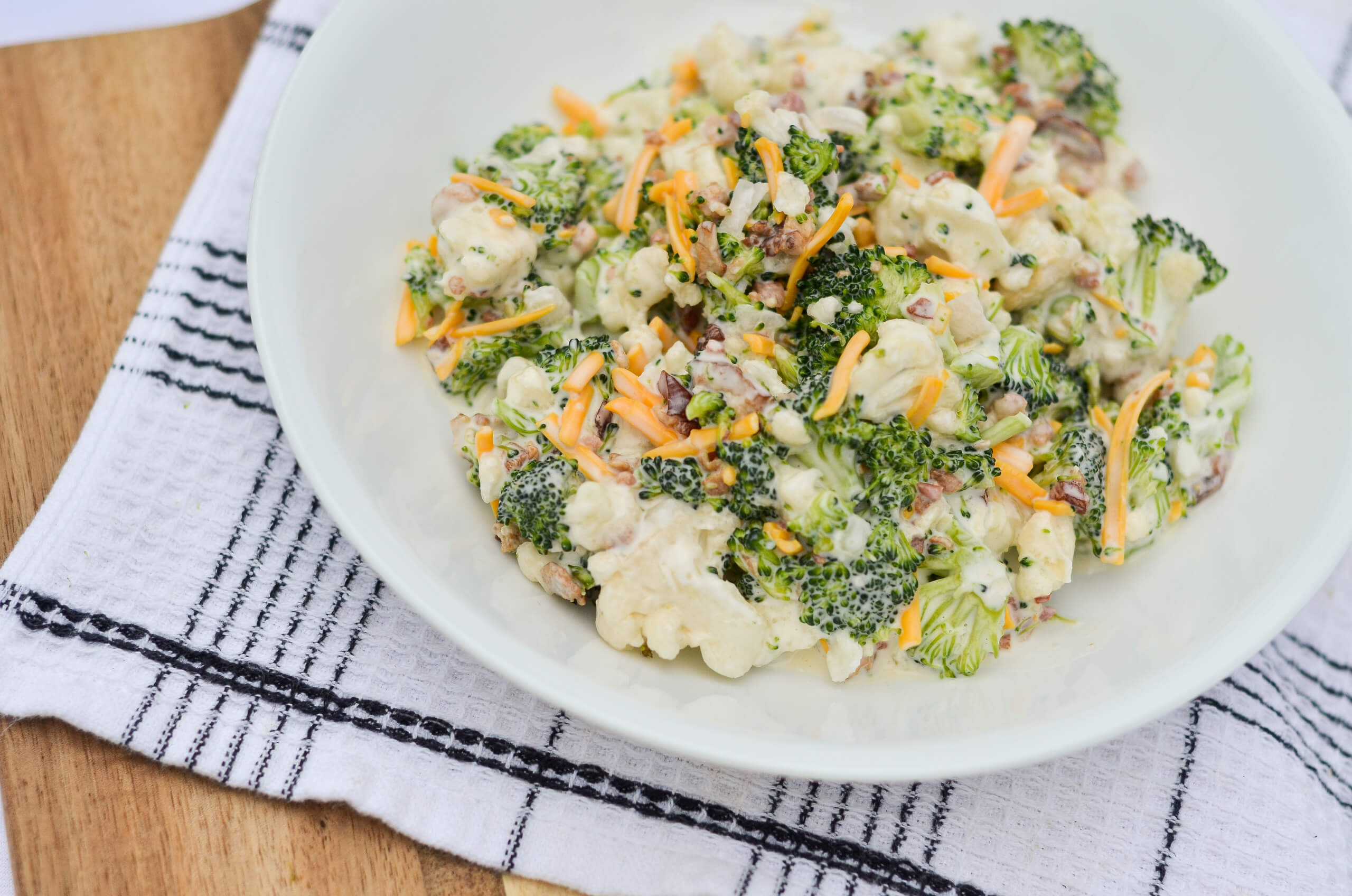 Nolt's Country Market Eldon, Missouri A white bowl filled with a salad made of broccoli, cauliflower, shredded carrots, sunflower seeds, and a creamy dressing sits on a checkered towel.