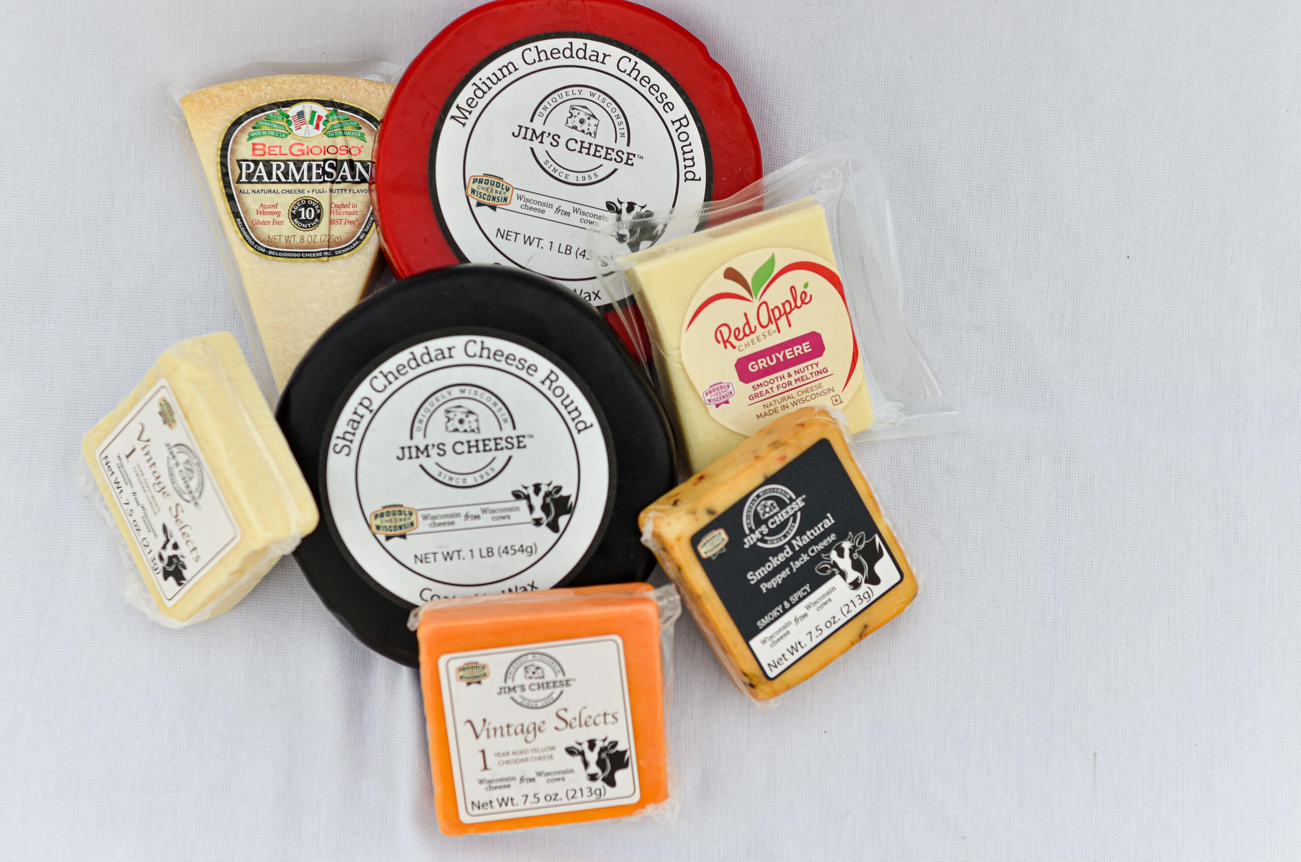 Nolt's Country Market Eldon, Missouri Assorted cheeses including cheddar, Parmesan, Gruyere, and Sharp Cheddar are arranged on a white surface, showing various packaging and labels.