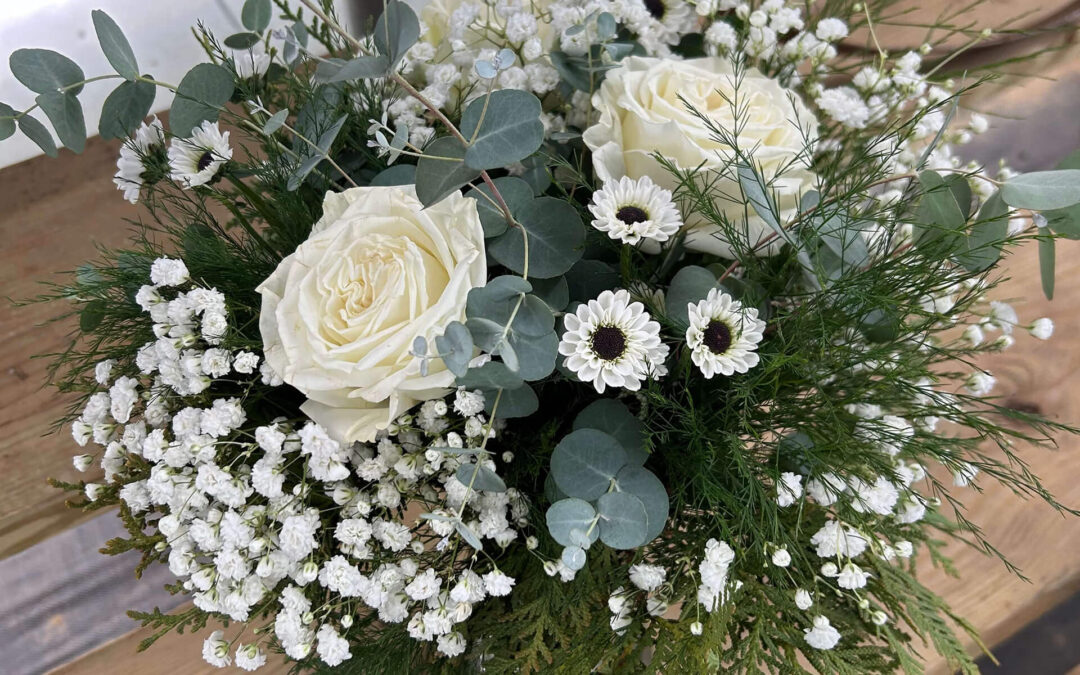 2.11.26 Swampy Hollow Greenhouse Valentines Gallery 5 A floral arrangement with white roses, baby's breath, small white daisies, eucalyptus, and greenery, placed on a wooden surface.