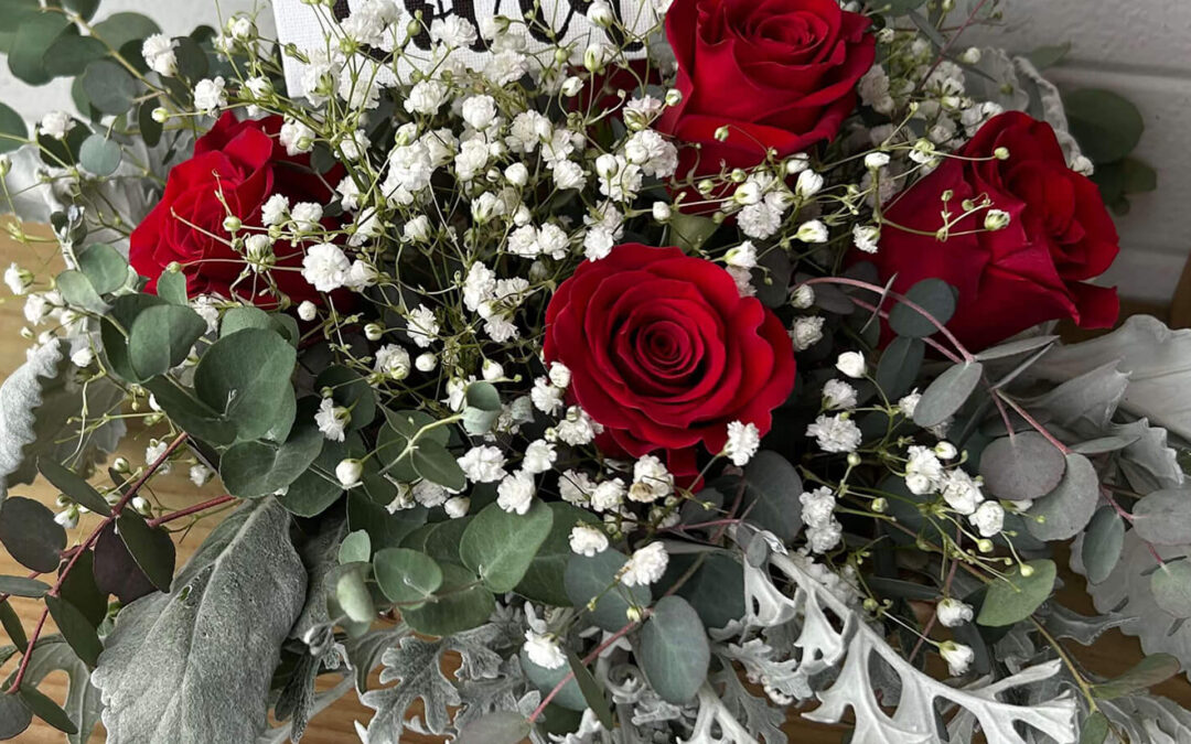 2.11.26 Swampy Hollow Greenhouse Valentines Gallery 8 A floral arrangement with three red roses, baby's breath, and assorted greenery, featuring a card that reads "You are loved.