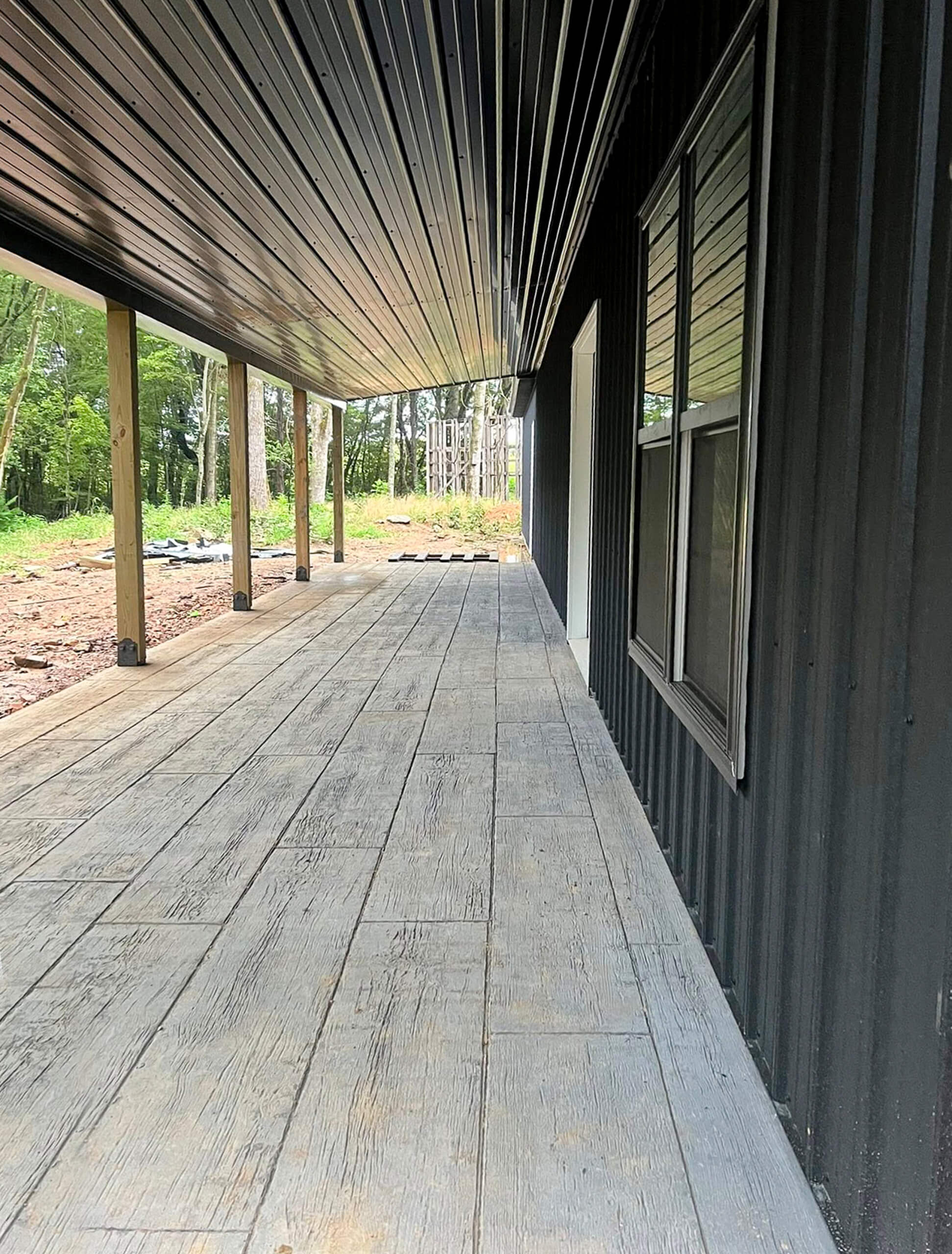 Bud's Construction Miunfordville KY A wooden porch with a slanted metal roof and black siding, featuring large windows and overlooking a grassy outdoor area.