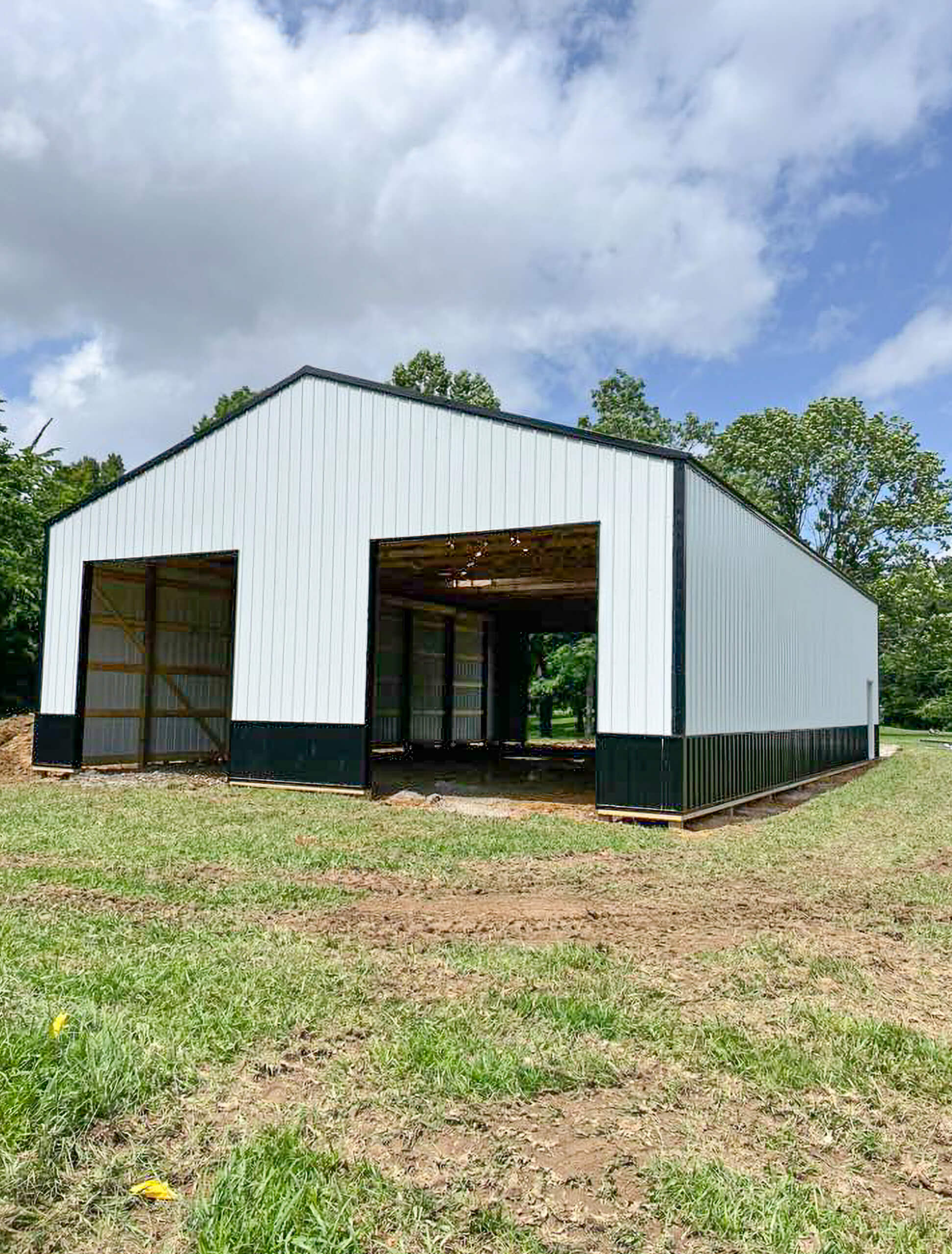 Bud's Construction Miunfordville KY A large, white metal building with open doorways stands on a grassy area under a partly cloudy sky.
