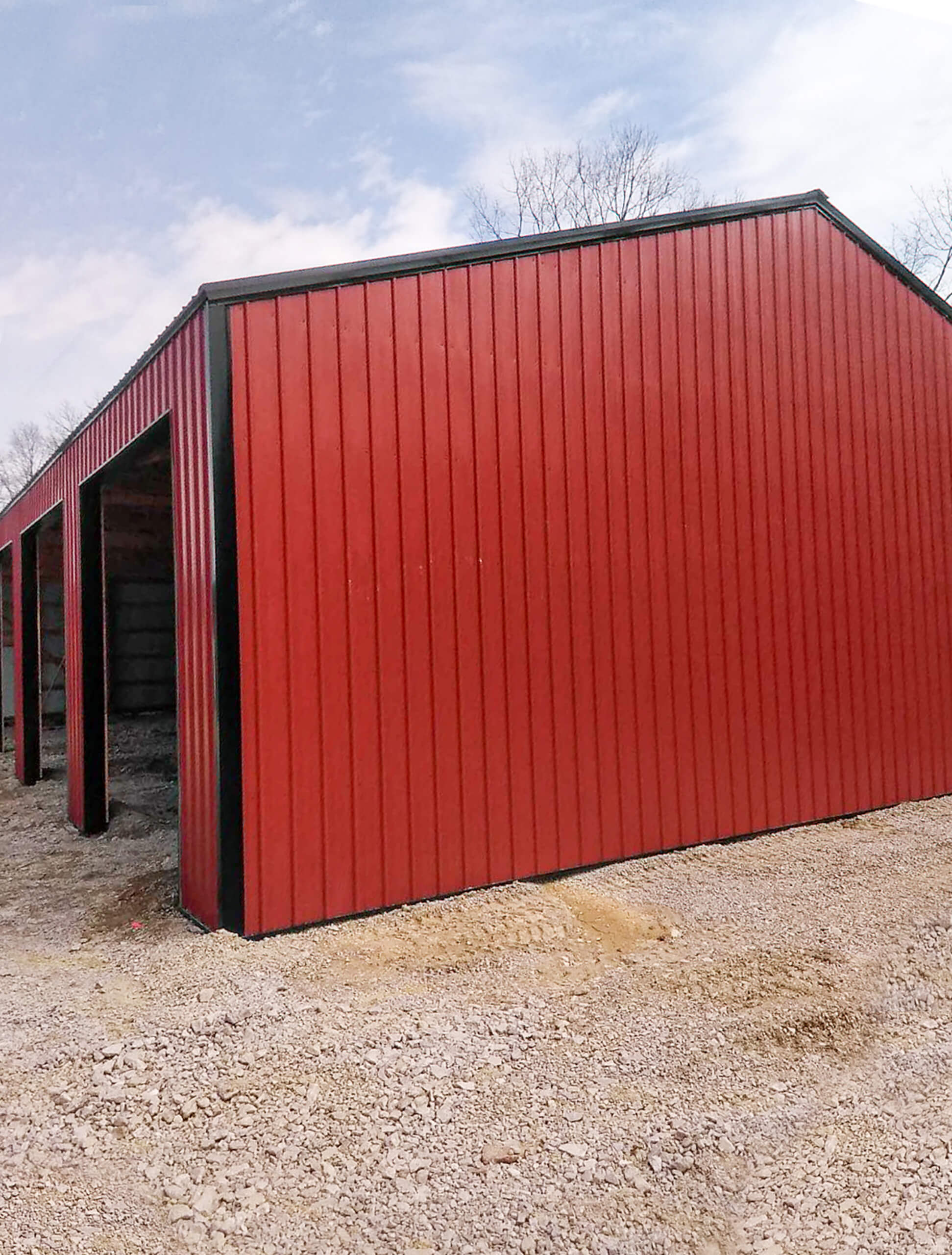 Bud's Construction Miunfordville KY A red metal building with open garage bays, standing on a gravel lot under a partly cloudy sky.