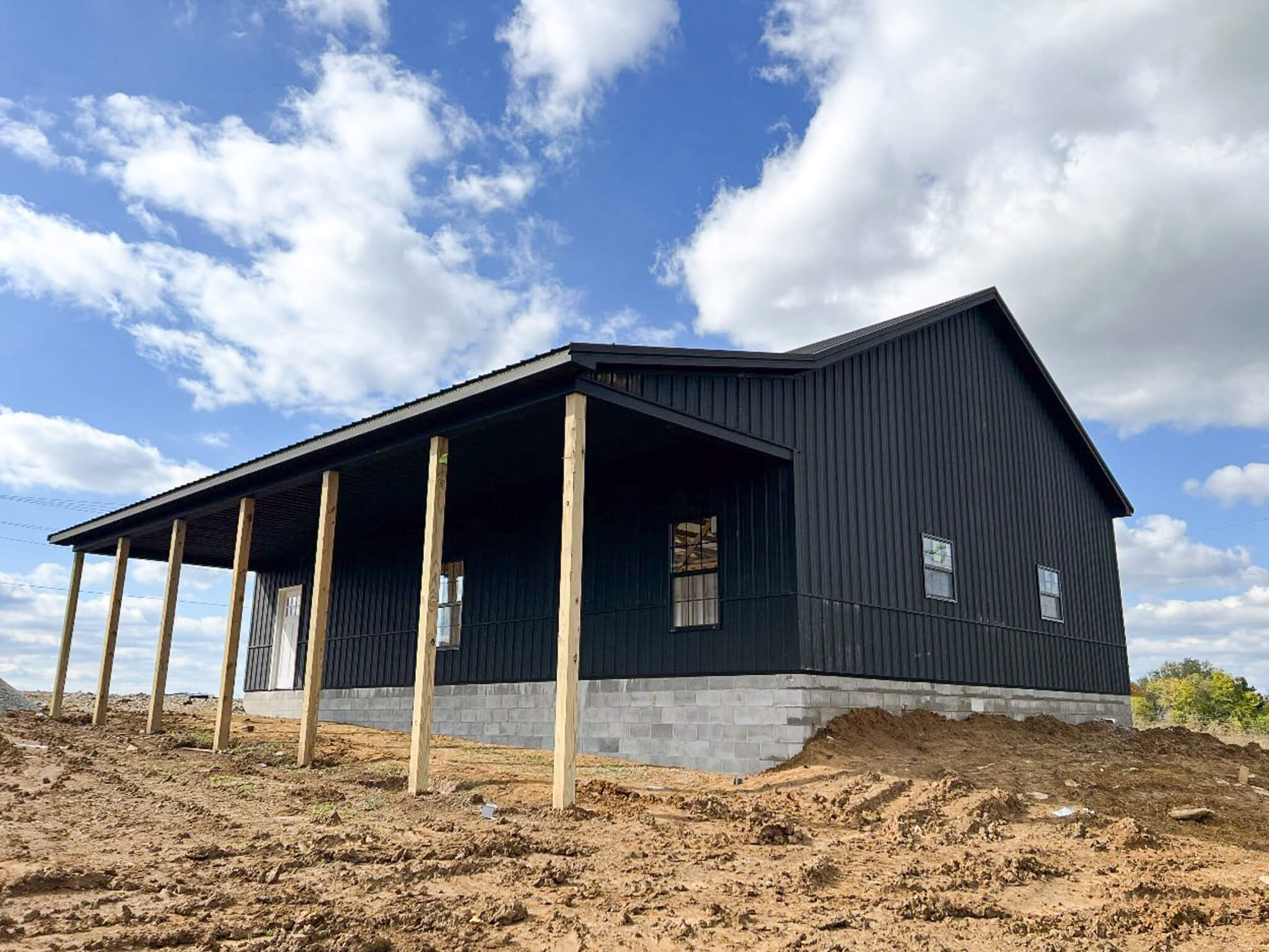 Bud's Construction Miunfordville KY A black metal building with a raised concrete foundation and unfinished porch stands on a dirt lot under a partly cloudy sky.