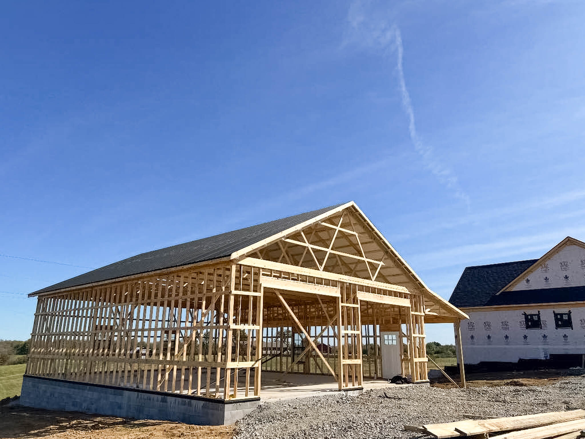 Bud's Construction Miunfordville KY A wooden frame structure of a building under construction beside a partially finished house on a clear, sunny day.