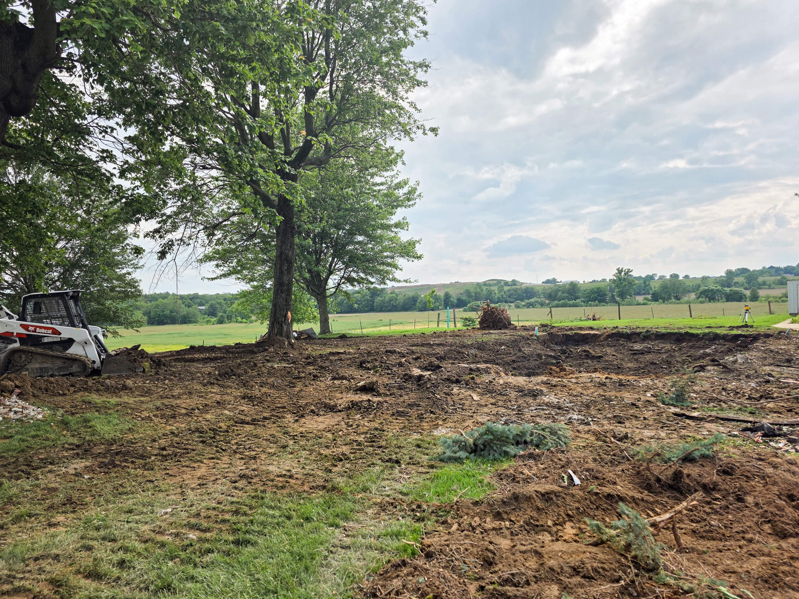 Elite Dumpster and Demolition Odon, IN A cleared plot of land with scattered debris, bordered by trees and open fields, and a small construction vehicle on the left.