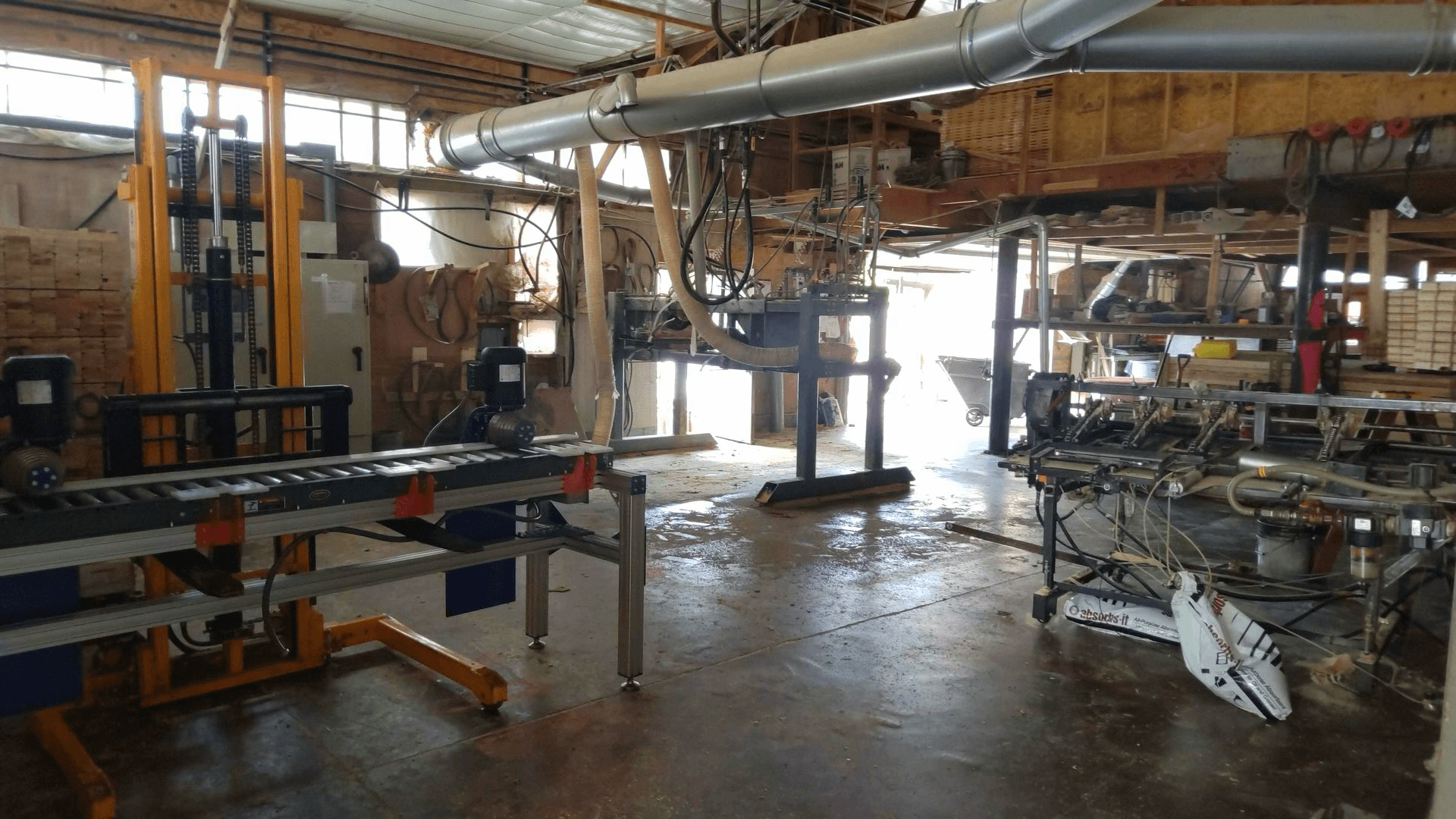 Industrial workshop interior with automated machinery, conveyor belts, and exposed wooden beams, showing equipment used for manufacturing or processing materials.