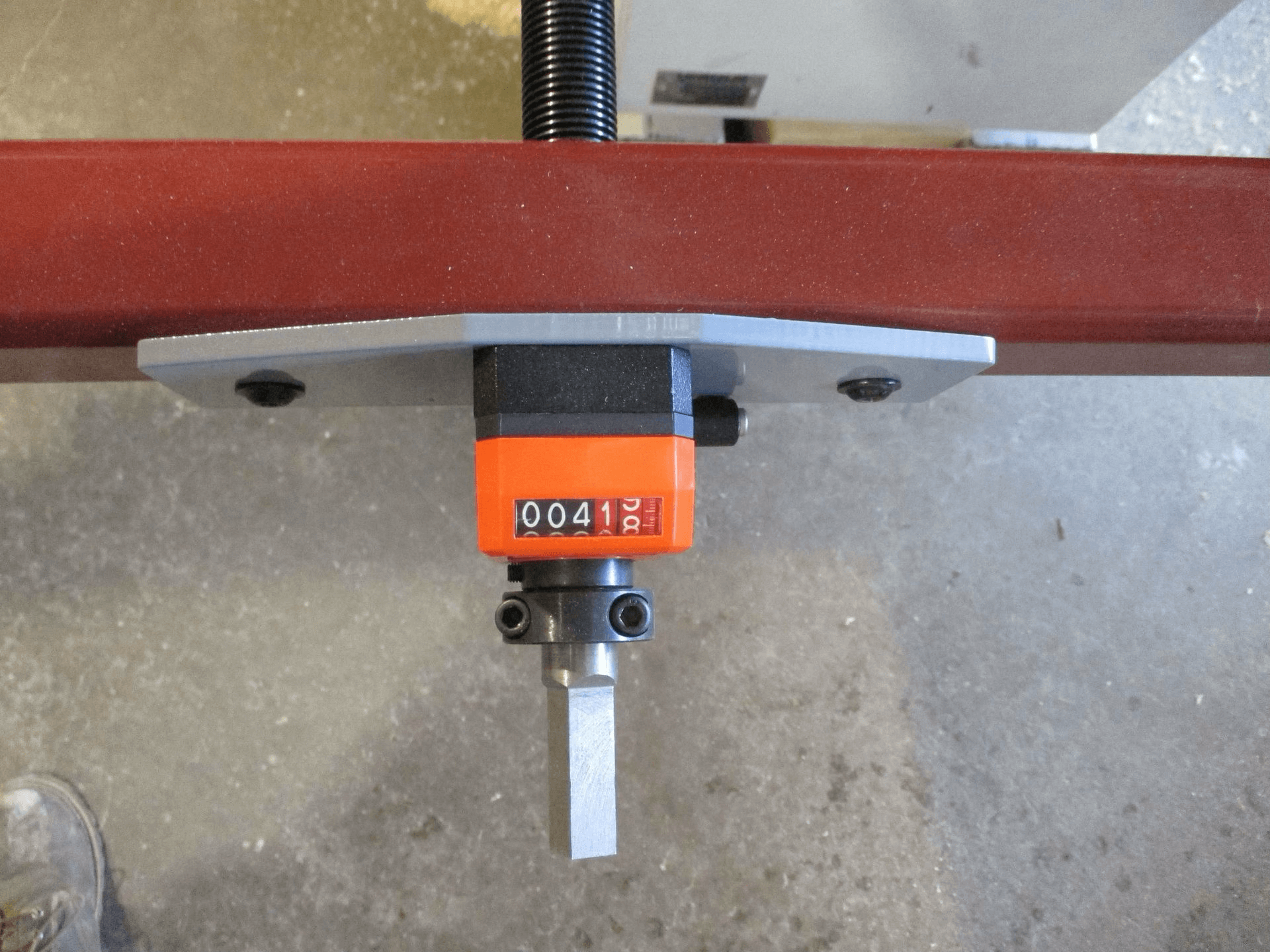Close-up of a mechanical counter device mounted on a metal bar, displaying the number 00412, with a gray concrete floor in the background.