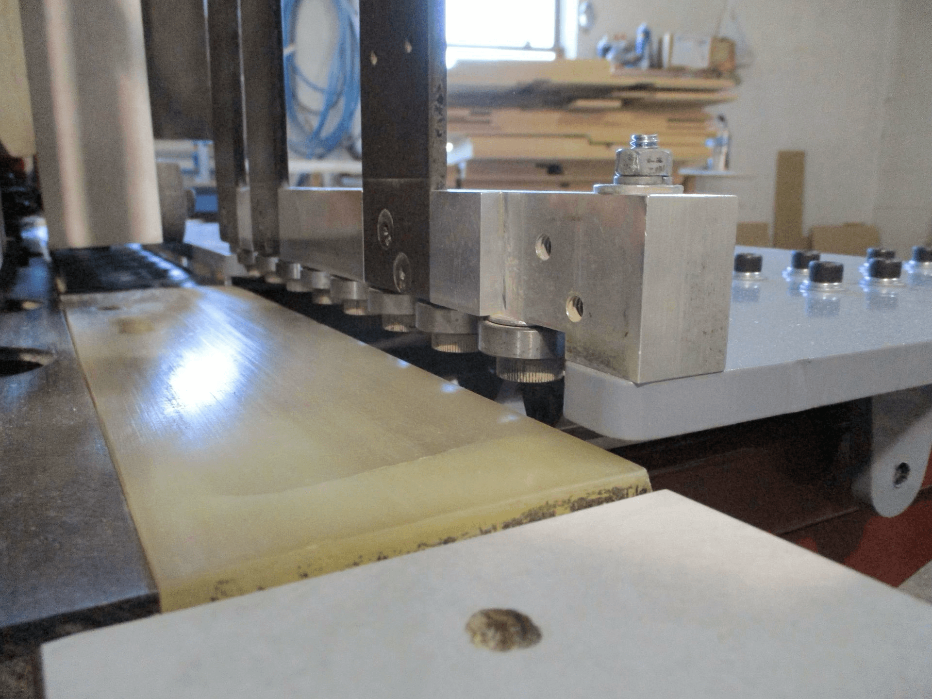Close-up of a woodworking machine drilling evenly spaced holes along the edge of a wooden board in a workshop.
