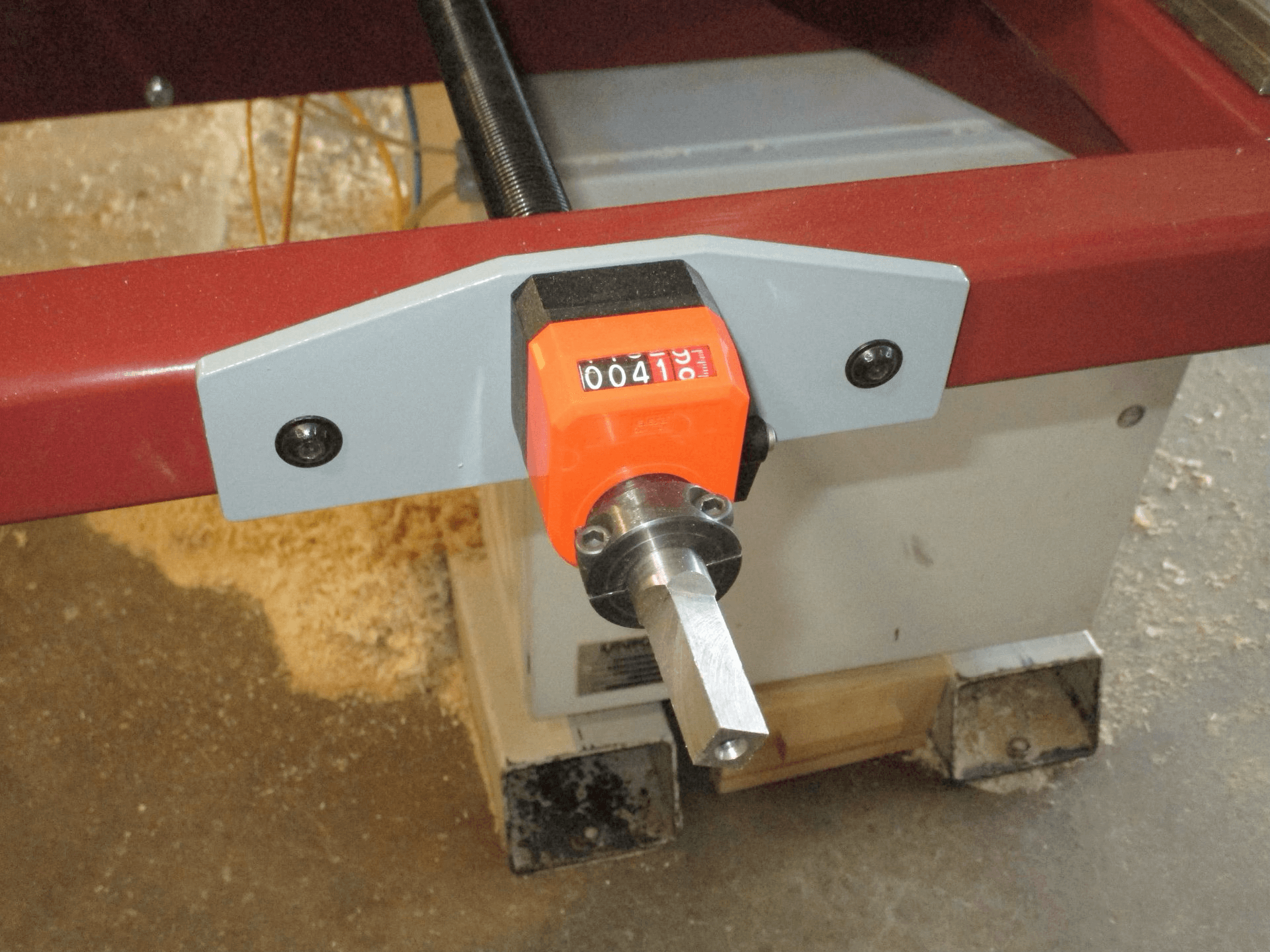 Close-up of a digital counter attached to a metal machine part, with wood shavings visible on the floor below.