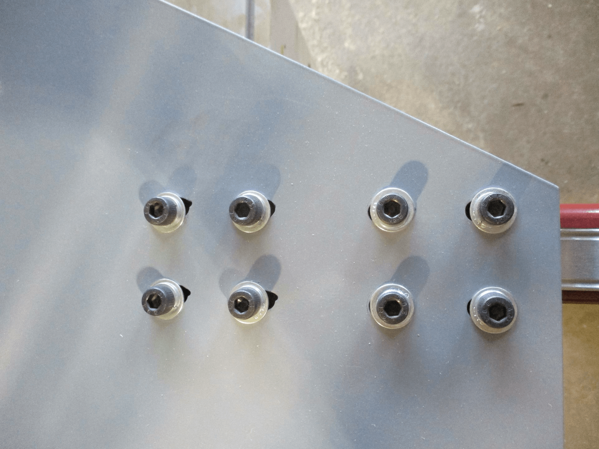 Eight evenly spaced bolts are fastened into a metallic surface, arranged in two columns and four rows.