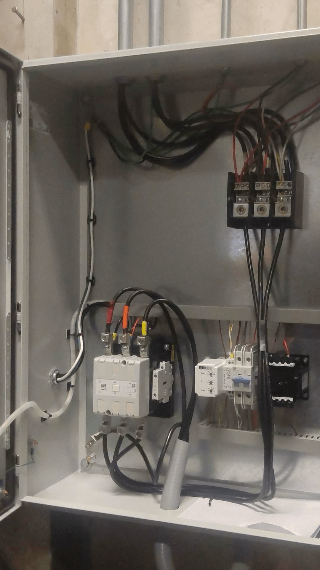 An open electrical control panel with various wires, circuit breakers, and terminals connected inside a metal enclosure.