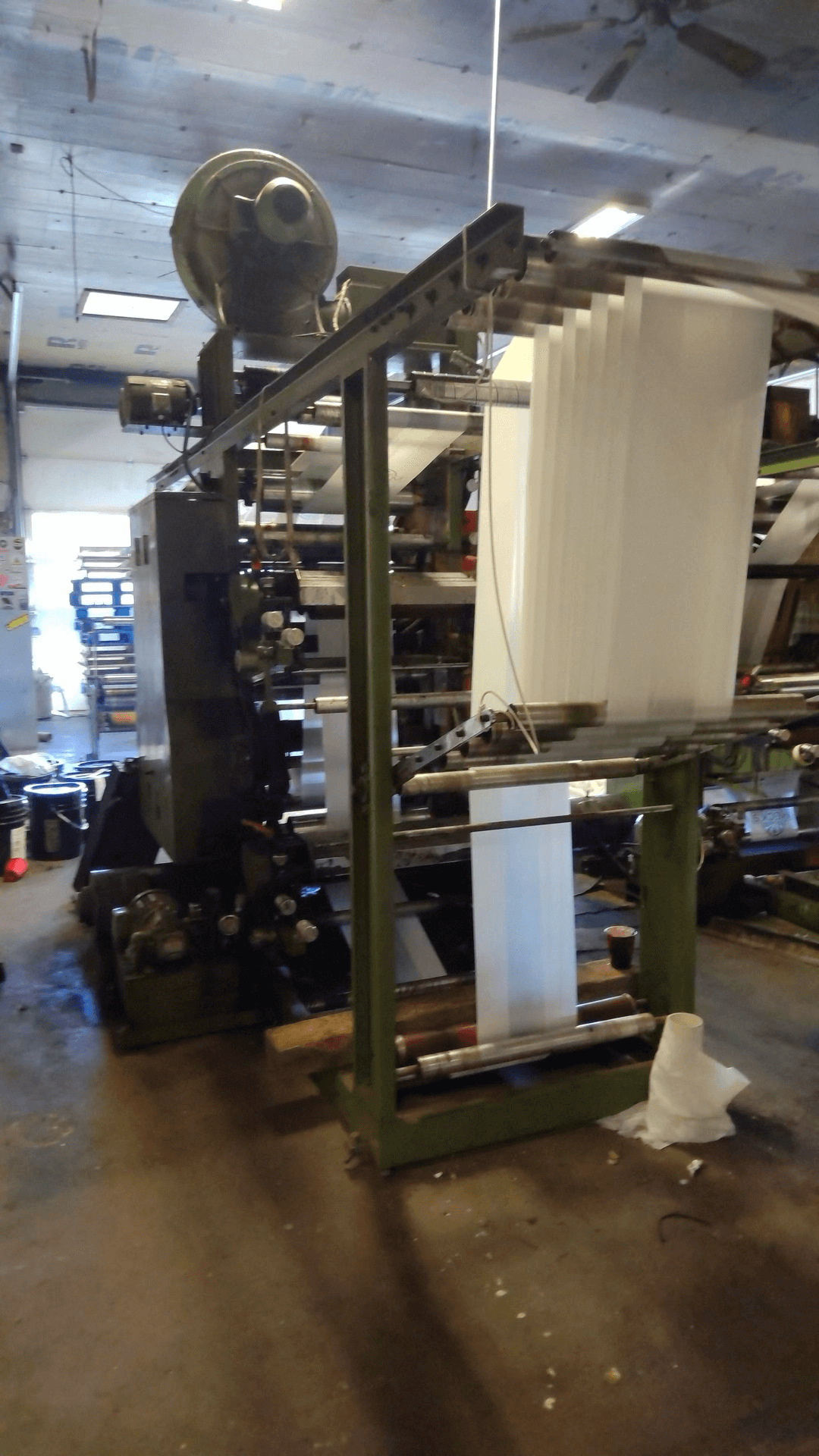 A large industrial machine with rolls of white material being fed through rollers in a factory setting.