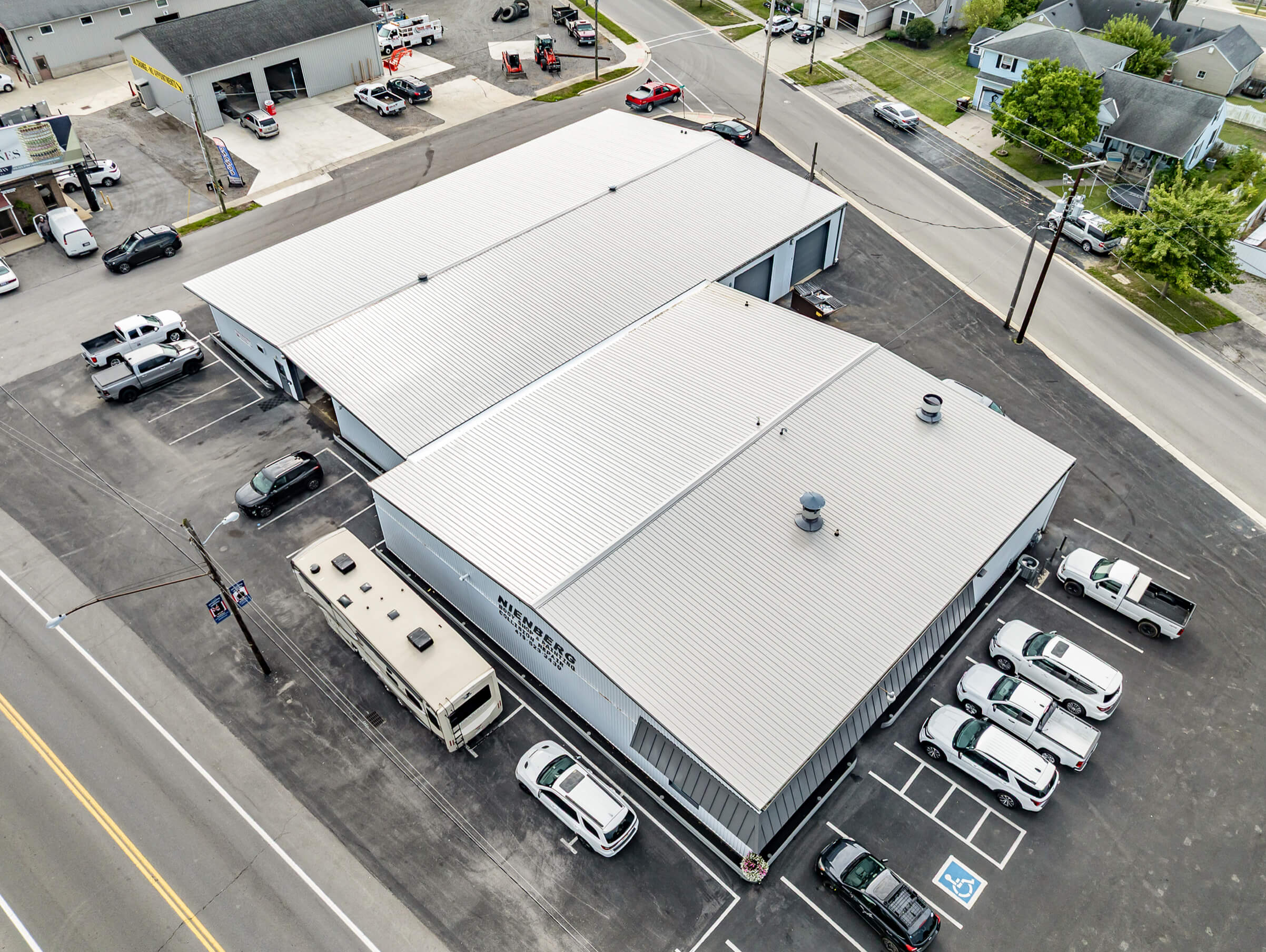 Cardinal Commercial Roofing Decatur IN Aerial view of a large industrial building with a metal roof, adjacent parking lot with cars and an RV, surrounded by roads and nearby commercial and residential properties.