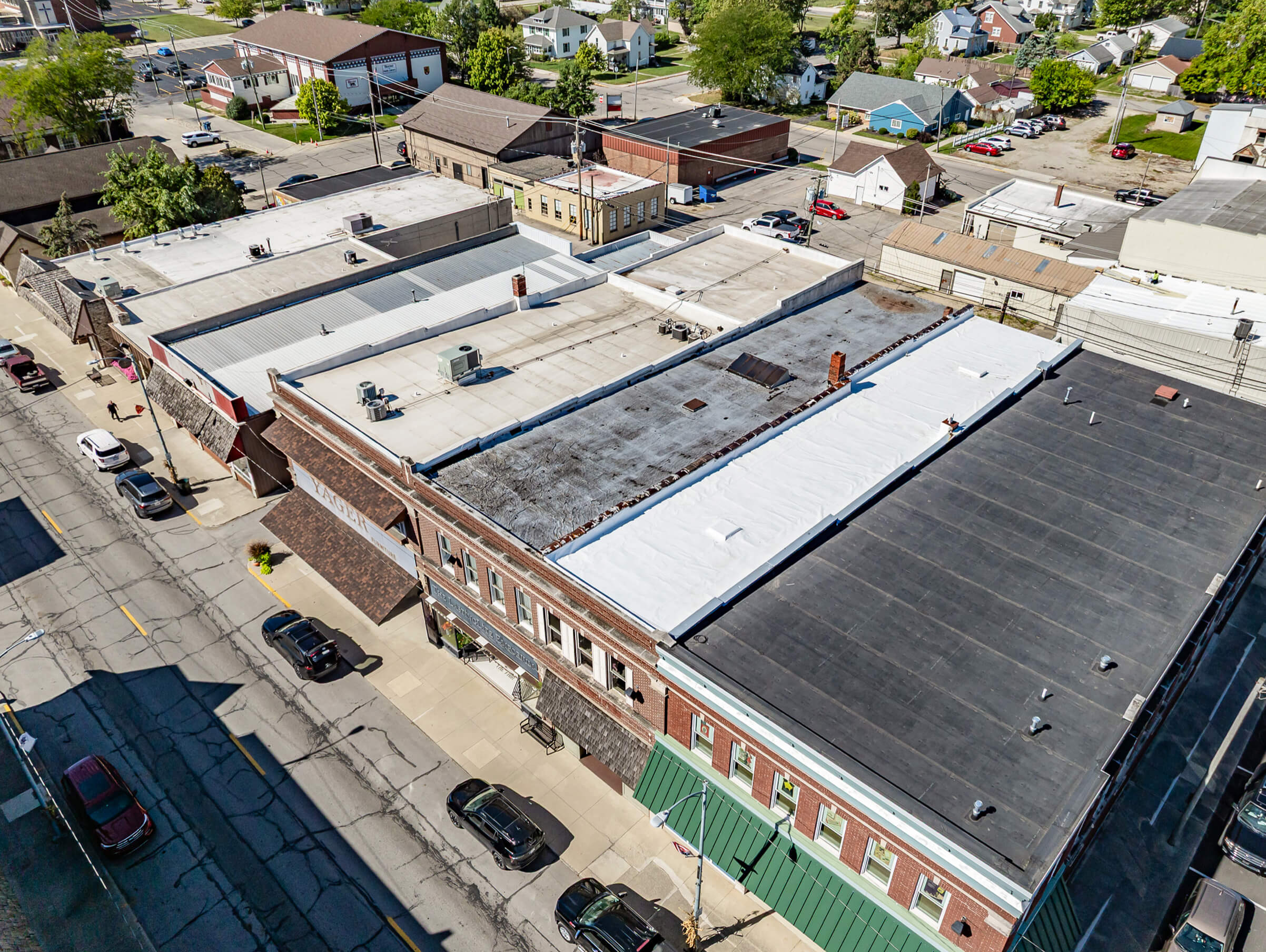 Cardinal Commercial Roofing Decatur IN Aerial view of a small town block with flat-roofed commercial buildings, parked cars along the street, and surrounding residential and business structures.