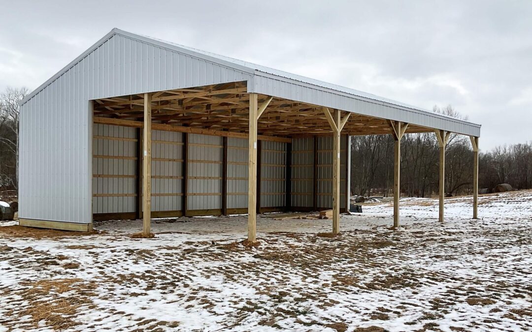 Amish Ridge Metals Mt Perry OH Open-sided metal and wood pole barn stands on snow-dusted ground under a cloudy sky, with trees in the background.
