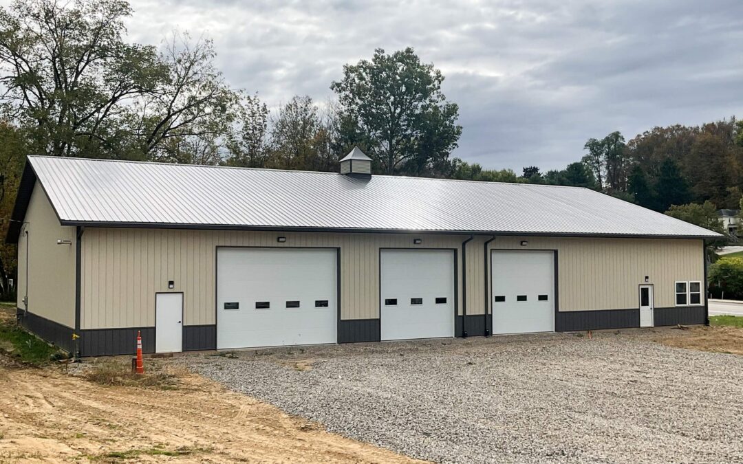 Amish Ridge Metals Mt Perry OH A large beige metal building with three white garage doors, a gravel driveway, and a cloudy sky in the background.