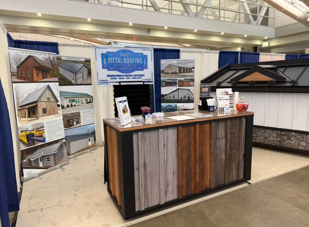 A trade show booth for Dave’s Metal Roofing featuring display panels, brochures, business cards, candy bowl, sample materials, and promotional signage.