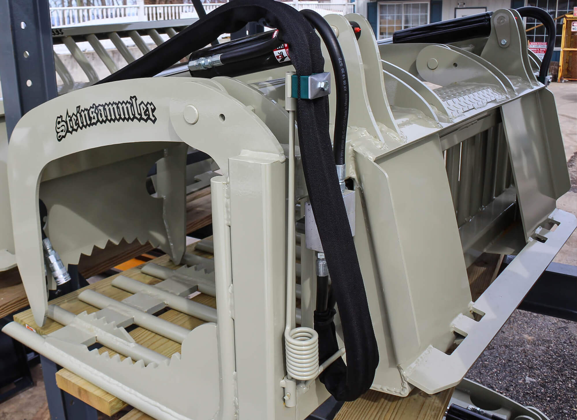 A heavy-duty metal grapple attachment for machinery labeled "Steinsammler," displayed on a wooden platform indoors.