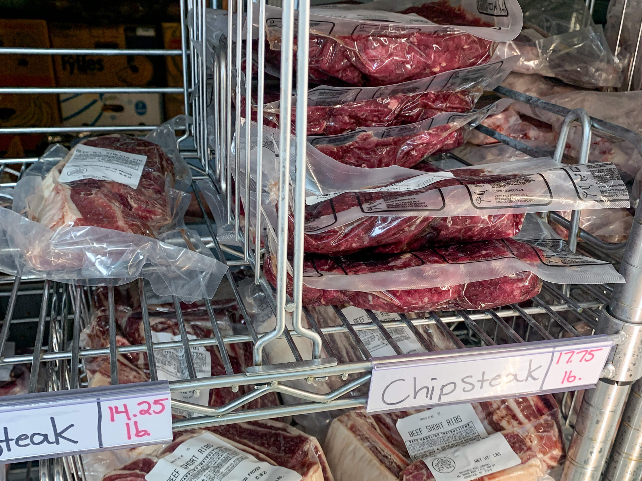 Maple Arch Farm Market Cochranville PA Packages of beef chip steak are stacked on metal shelves in a refrigerated display, with handwritten price tags below showing $14.25/lb and $17.75/lb.