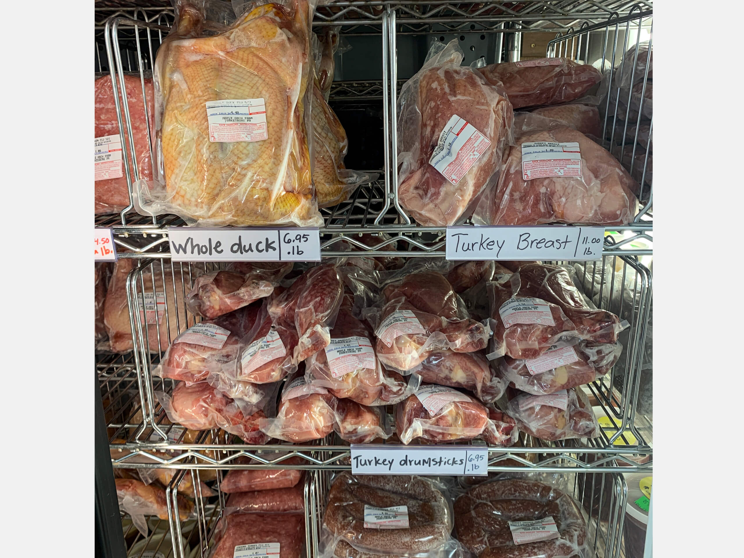 Maple Arch Farm Market Cochranville PA Vacuum-packed whole duck, turkey breast, and turkey drumsticks are displayed on metal shelves with handwritten labels and prices.