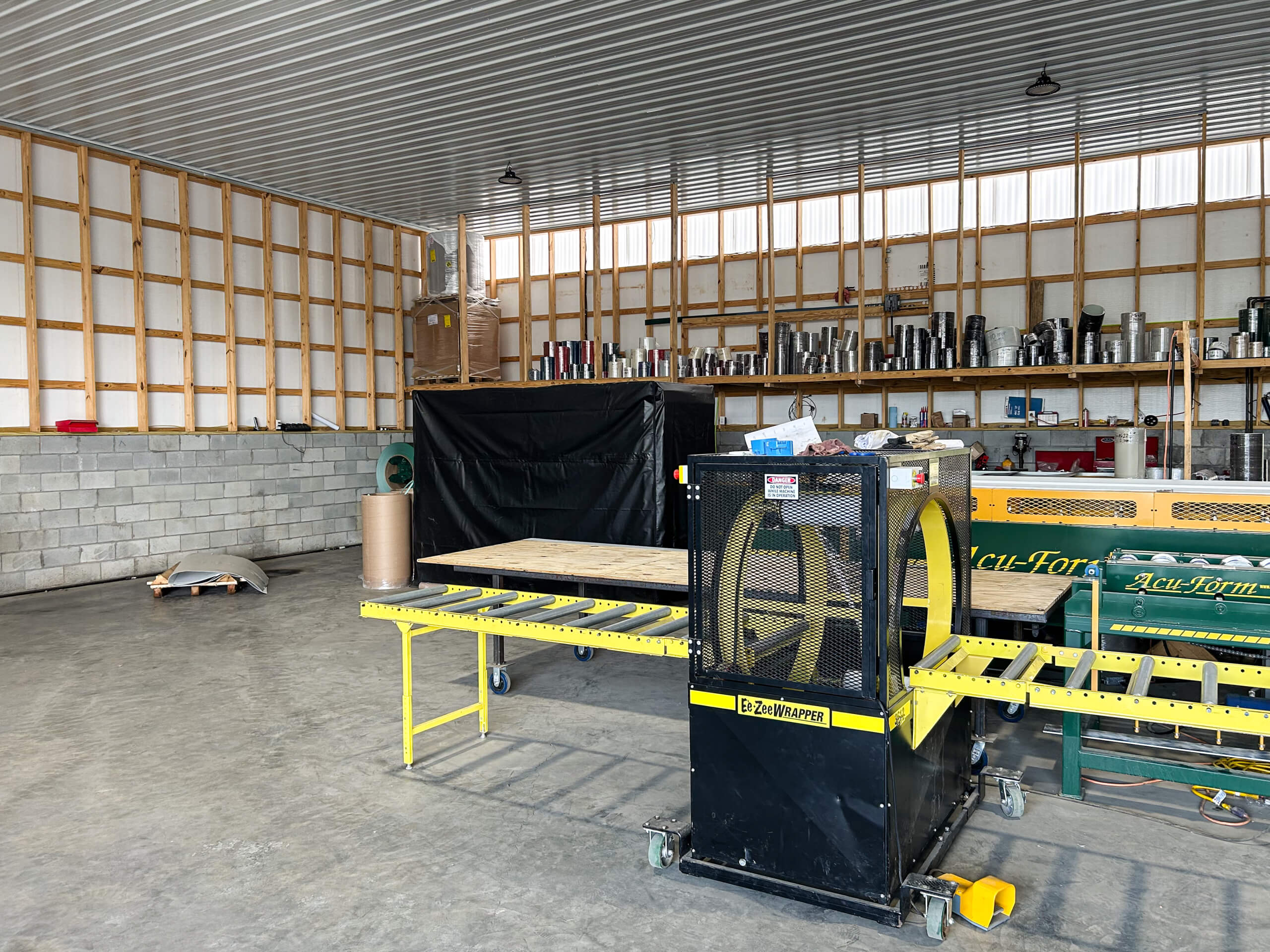 Metal Profiles Rose Hill, VA A large workshop with exposed framing and shelving, containing industrial equipment, tools, a strapping machine, and materials organized along the walls.