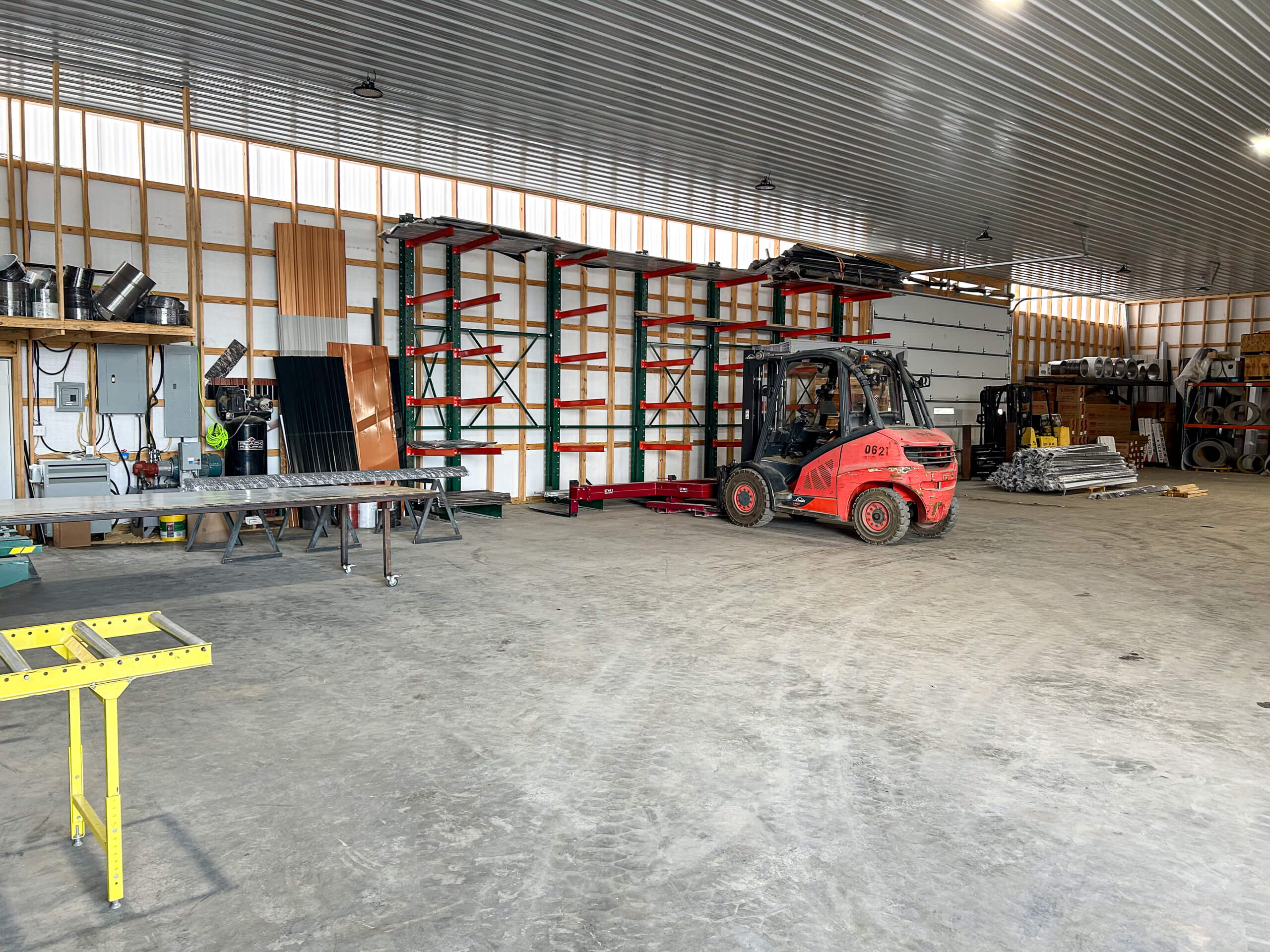 Metal Profiles Rose Hill, VA A red forklift is parked inside a spacious warehouse with metal shelves, worktables, construction materials, and equipment along the walls.