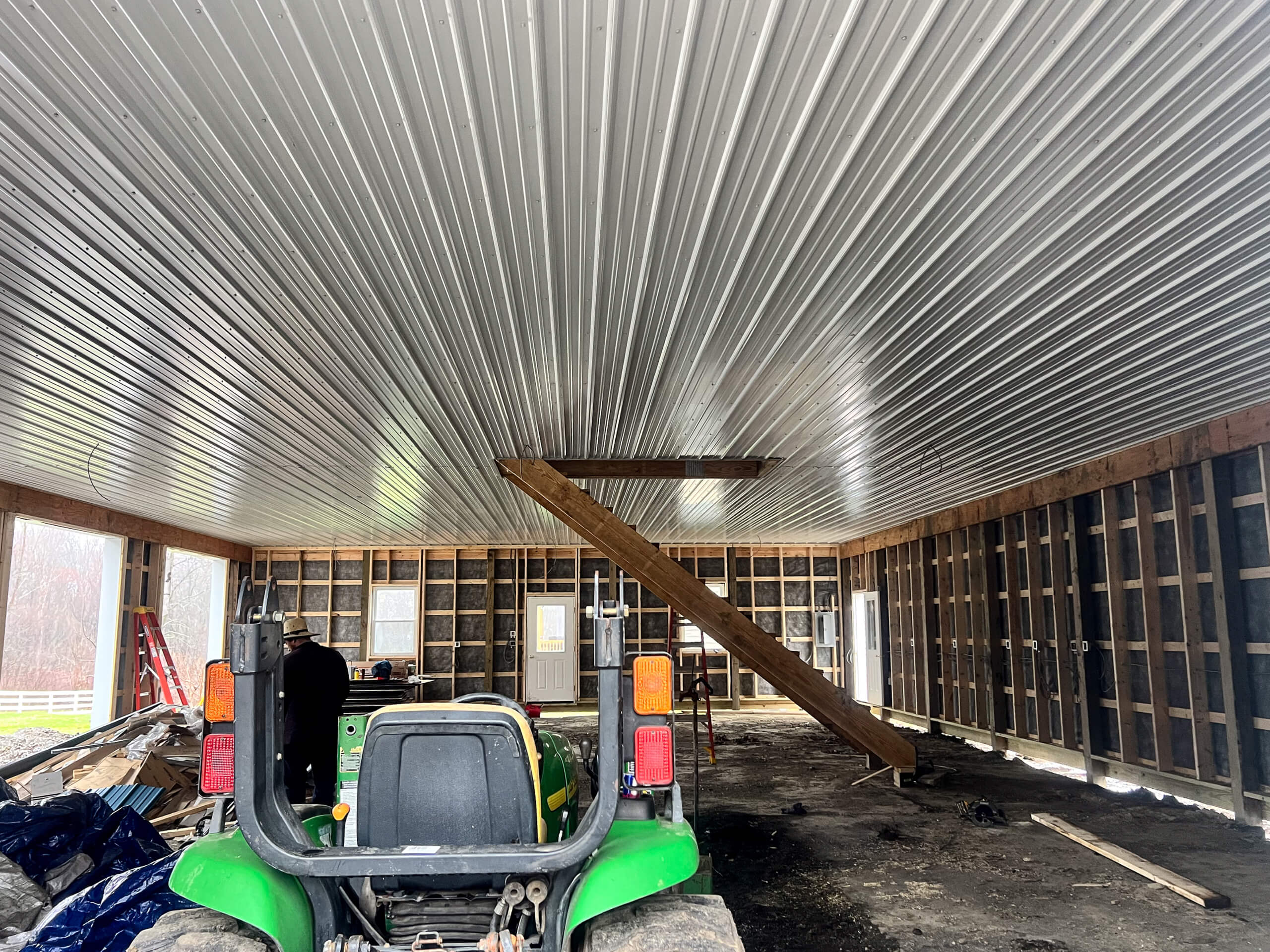 Crawford County Roofing Spartasburg PA A partially constructed building with exposed wooden framing, a corrugated metal ceiling, and a green utility vehicle parked inside; a wooden ramp is propped against the ceiling.