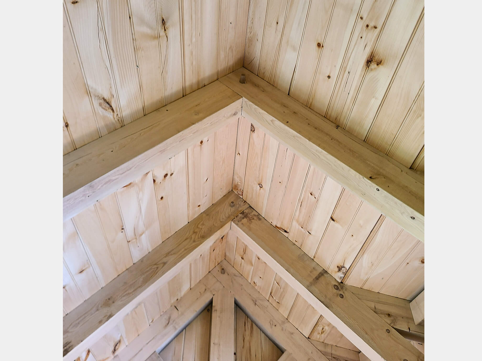 Elite Timberframes Canastota, NY Close-up view of a wooden vaulted ceiling with exposed beams and light-colored wood paneling.