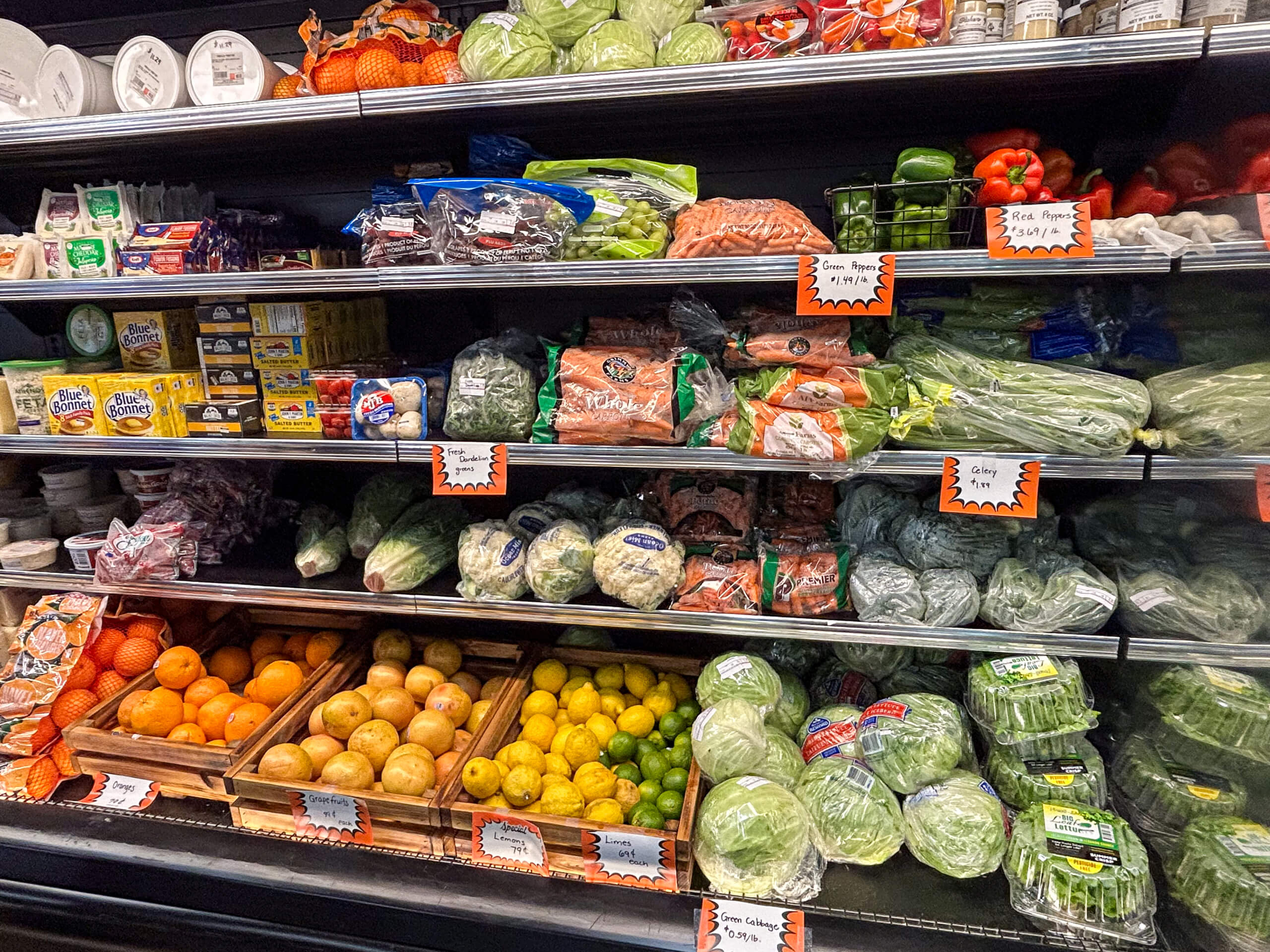 Jamar Groceries Kutztown PA Shelves stocked with fresh produce including lettuce, carrots, peppers, citrus fruits, and packaged greens, alongside dairy and deli items in a grocery store.