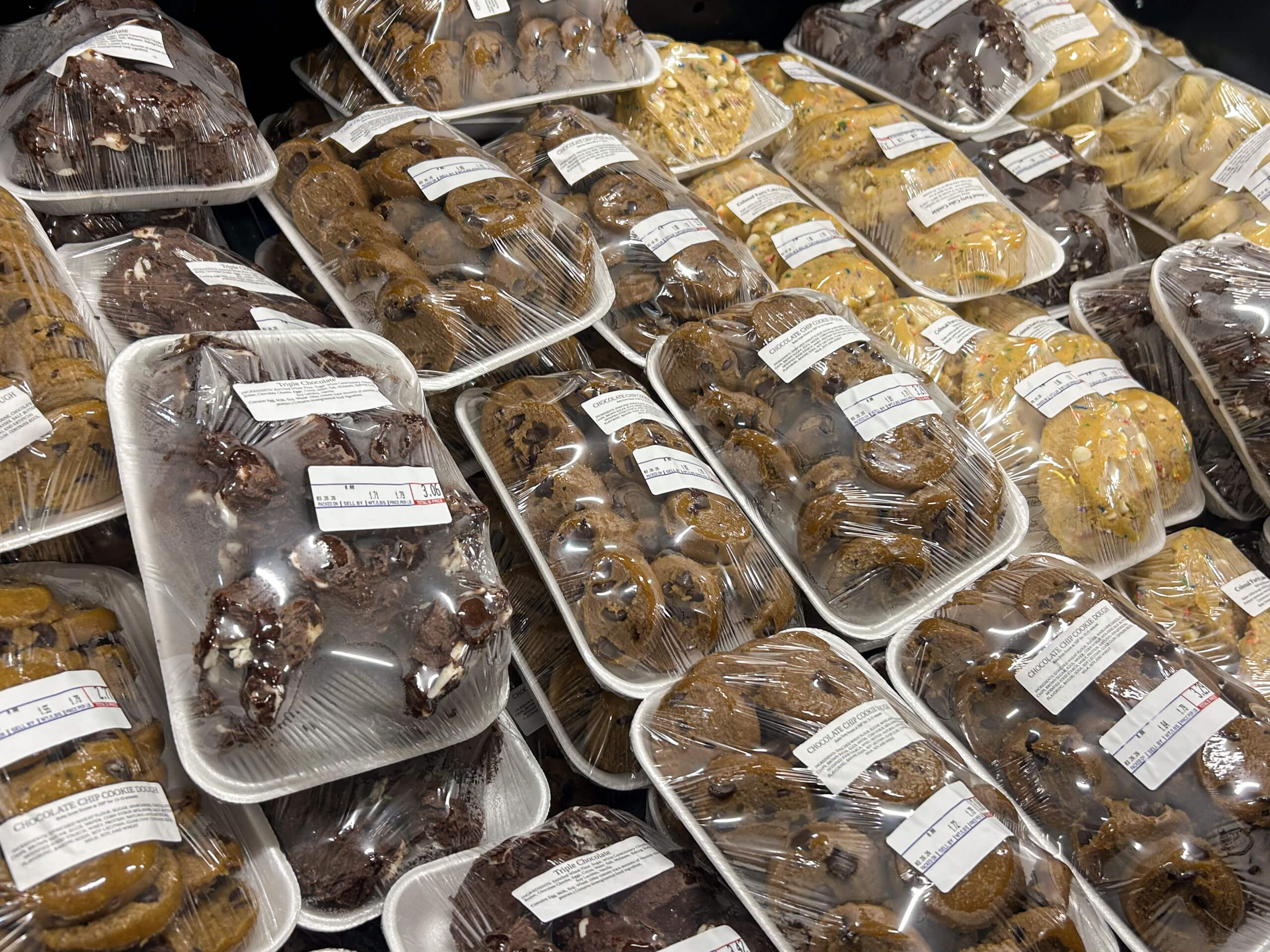 Jamar Groceries Kutztown PA Plastic-wrapped trays of assorted cookies are stacked for sale, each with a printed label and barcode visible on the packaging.