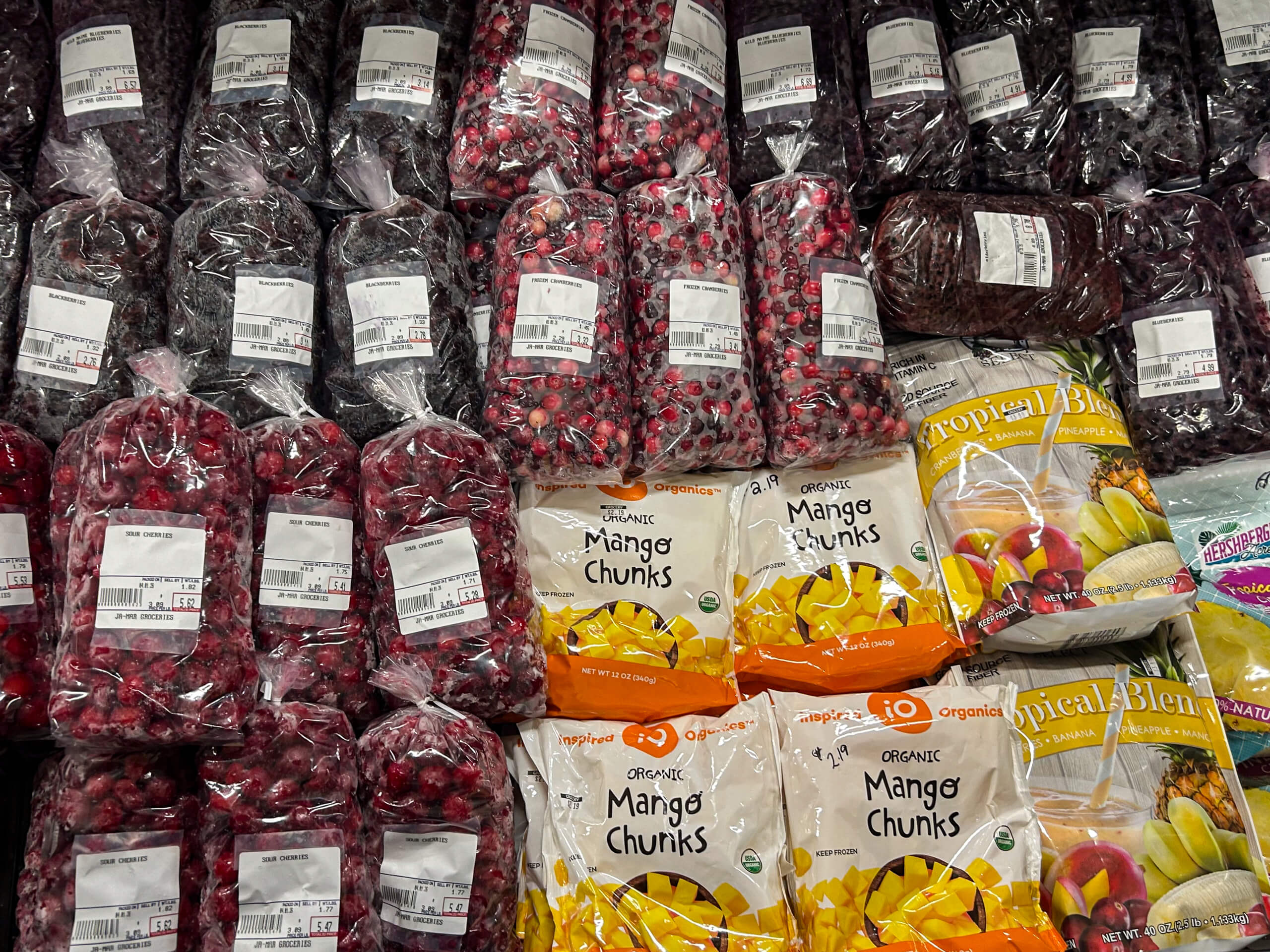 Jamar Groceries Kutztown PA Bags of frozen cherries and berries are stacked above bags of frozen mango chunks and fruit blend in a grocery store freezer section.