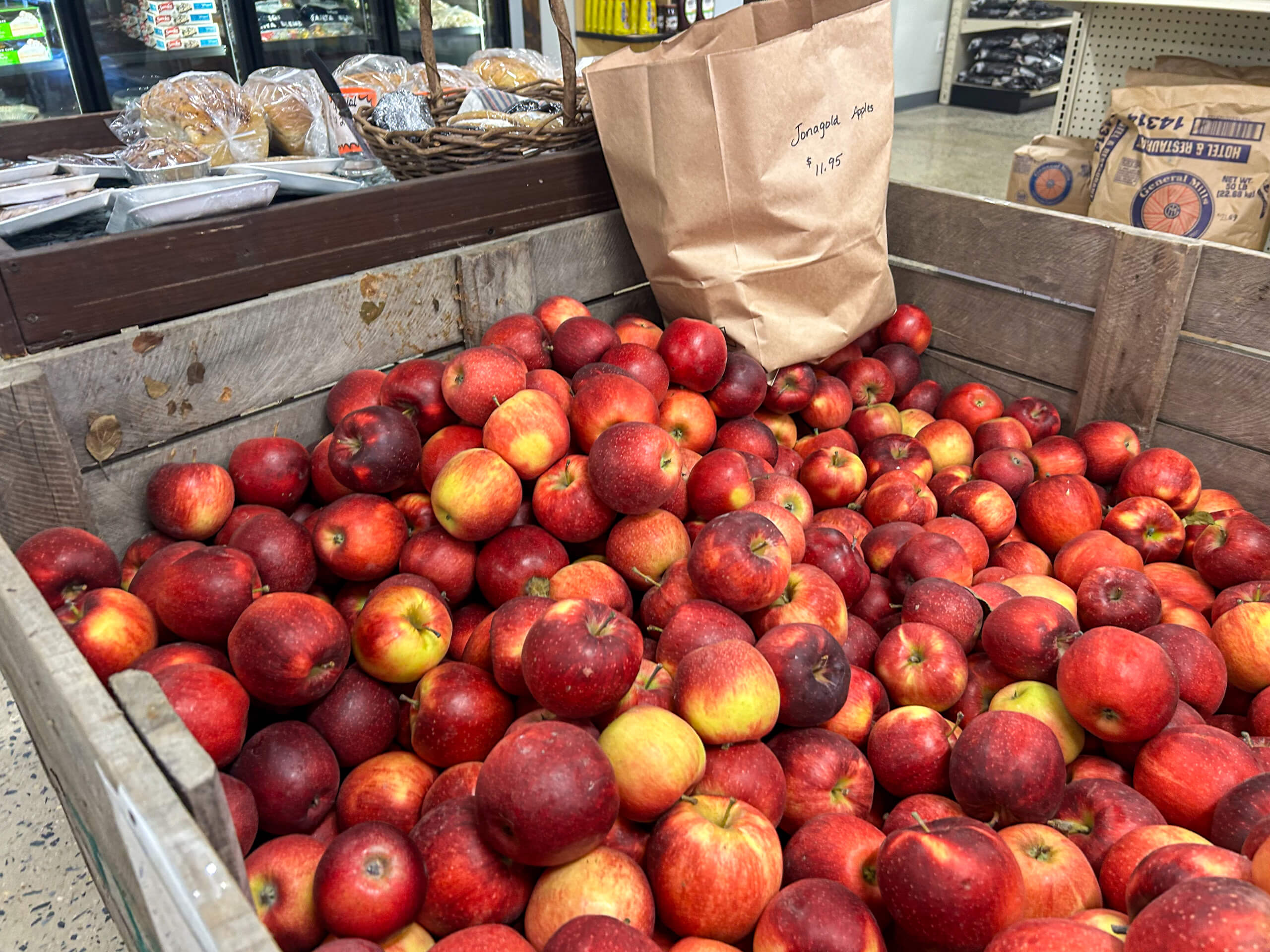 Jamar Groceries Kutztown PA A wooden bin filled with red apples sits in a grocery store, with a brown paper bag labeled "Empire Apples" priced at $1.85 nearby.