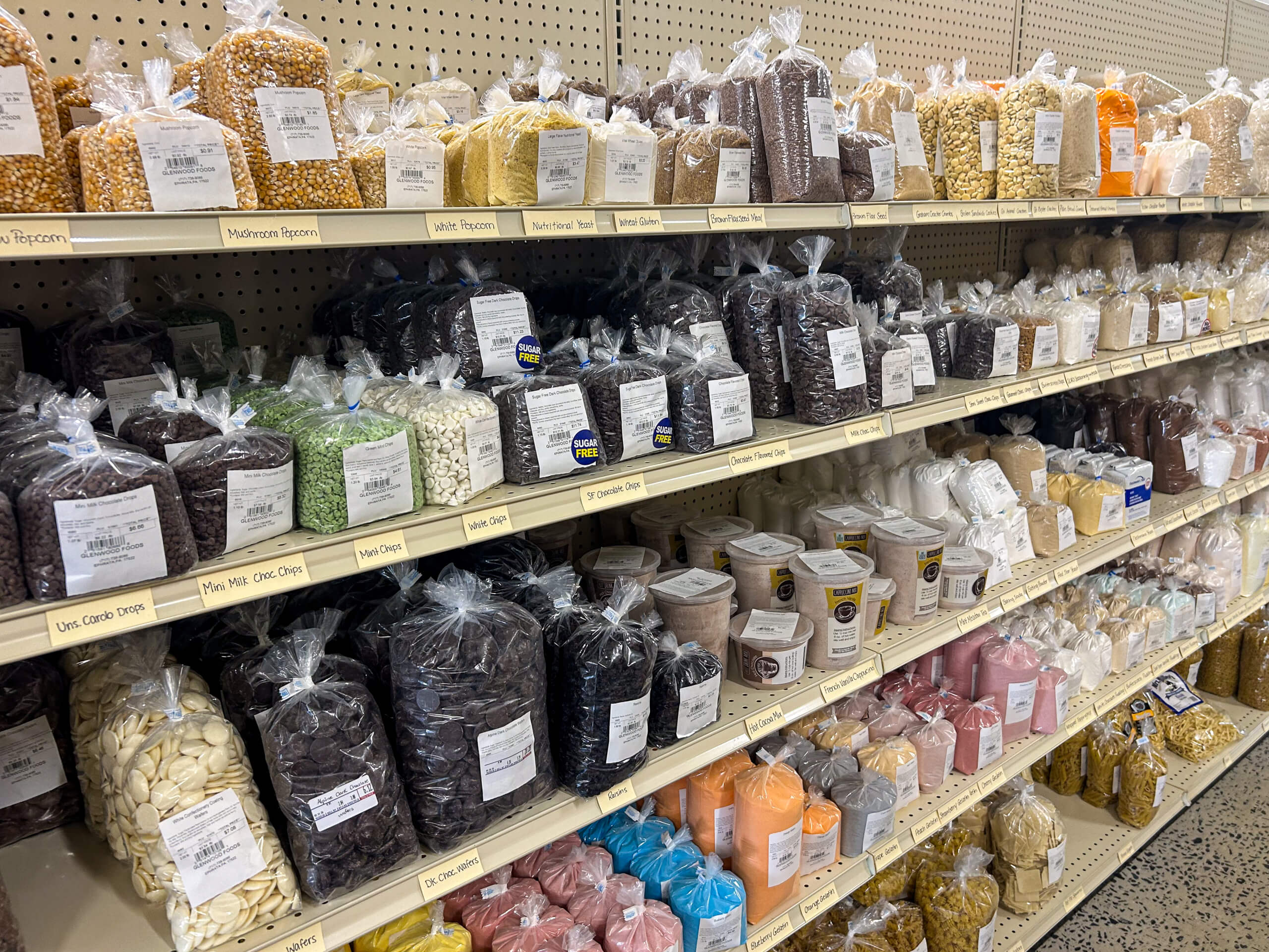 Jamar Groceries Kutztown PA Bags of dried beans, lentils, and grains are neatly arranged on shelves in a grocery store bulk foods section.