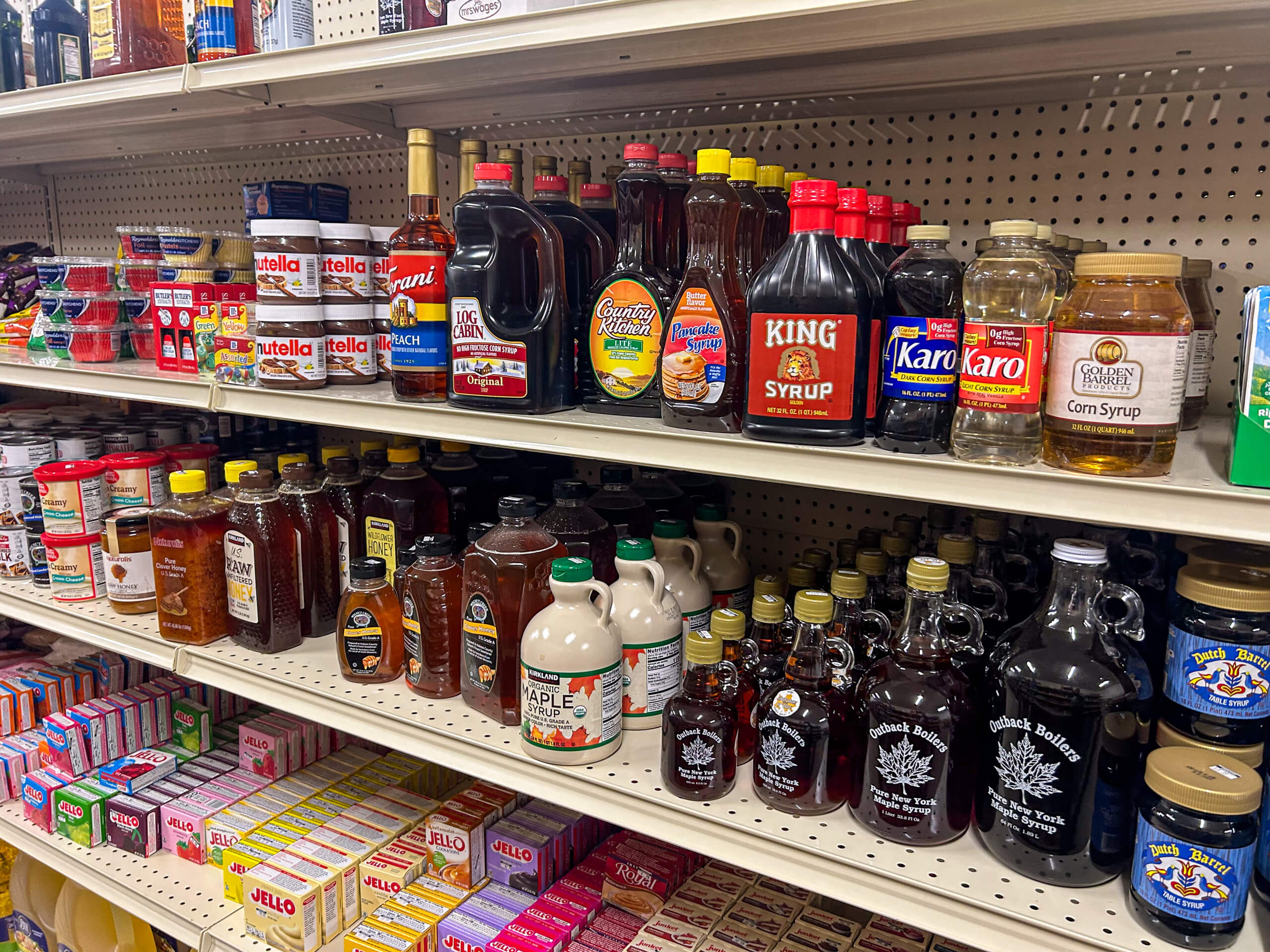 Jamar Groceries Kutztown PA Shelves stocked with various syrups, honey, and spreads in glass and plastic bottles and jars at a grocery store.