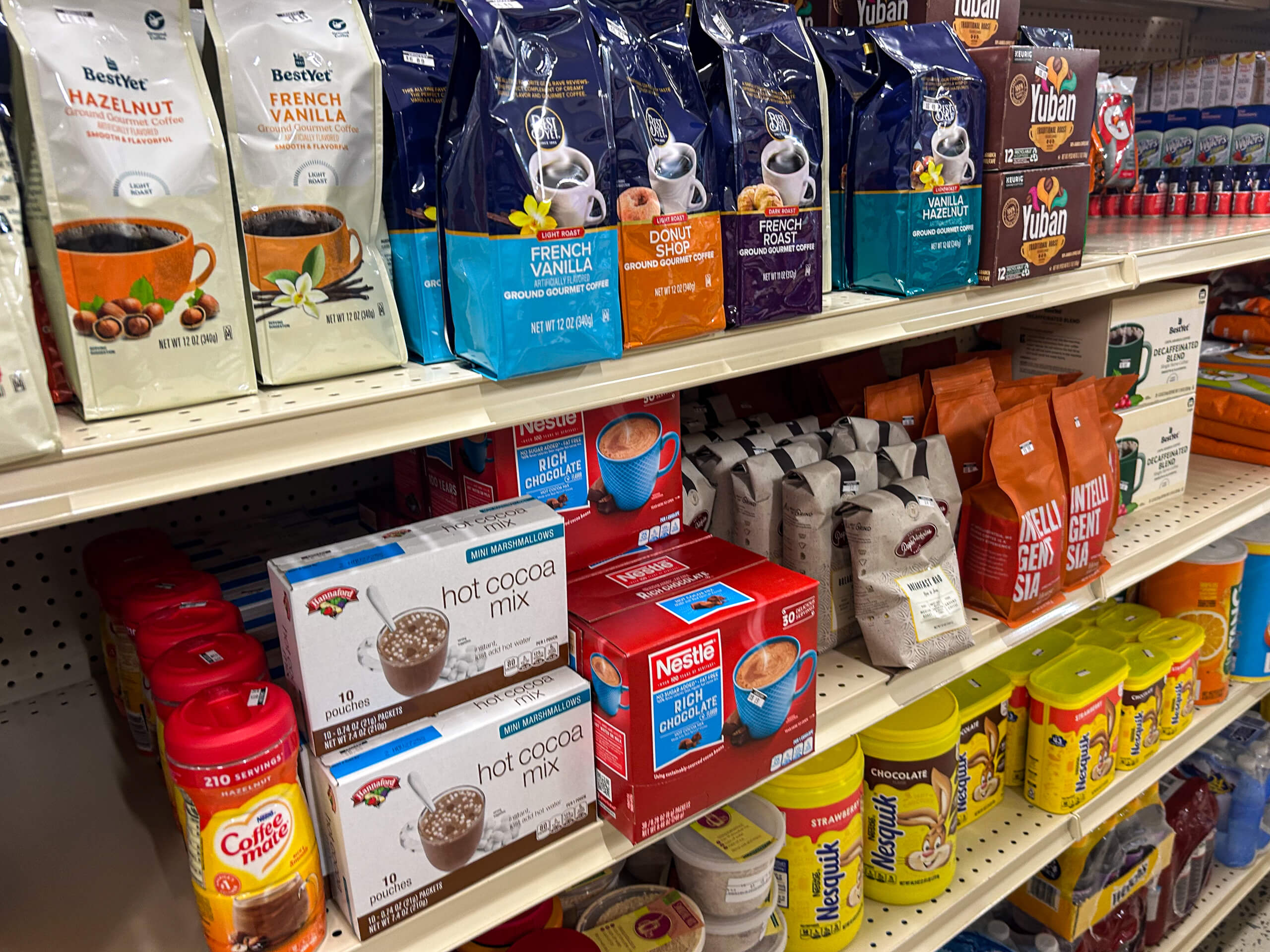 Jamar Groceries Kutztown PA Grocery store shelf stocked with various coffee bags, hot cocoa mix boxes, and powdered creamers arranged in rows.