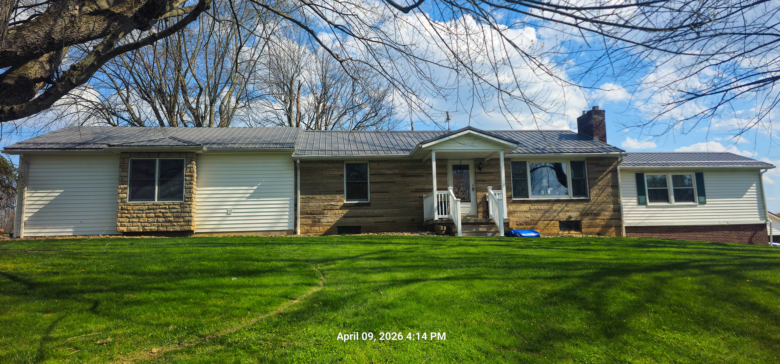 Nelson Weaver Metal Roofing Carrollton OH A single-story house with mixed siding and a small front porch sits on a grassy lawn under a partly cloudy sky. Date and time stamp: April 09, 2024, 4:14 PM.