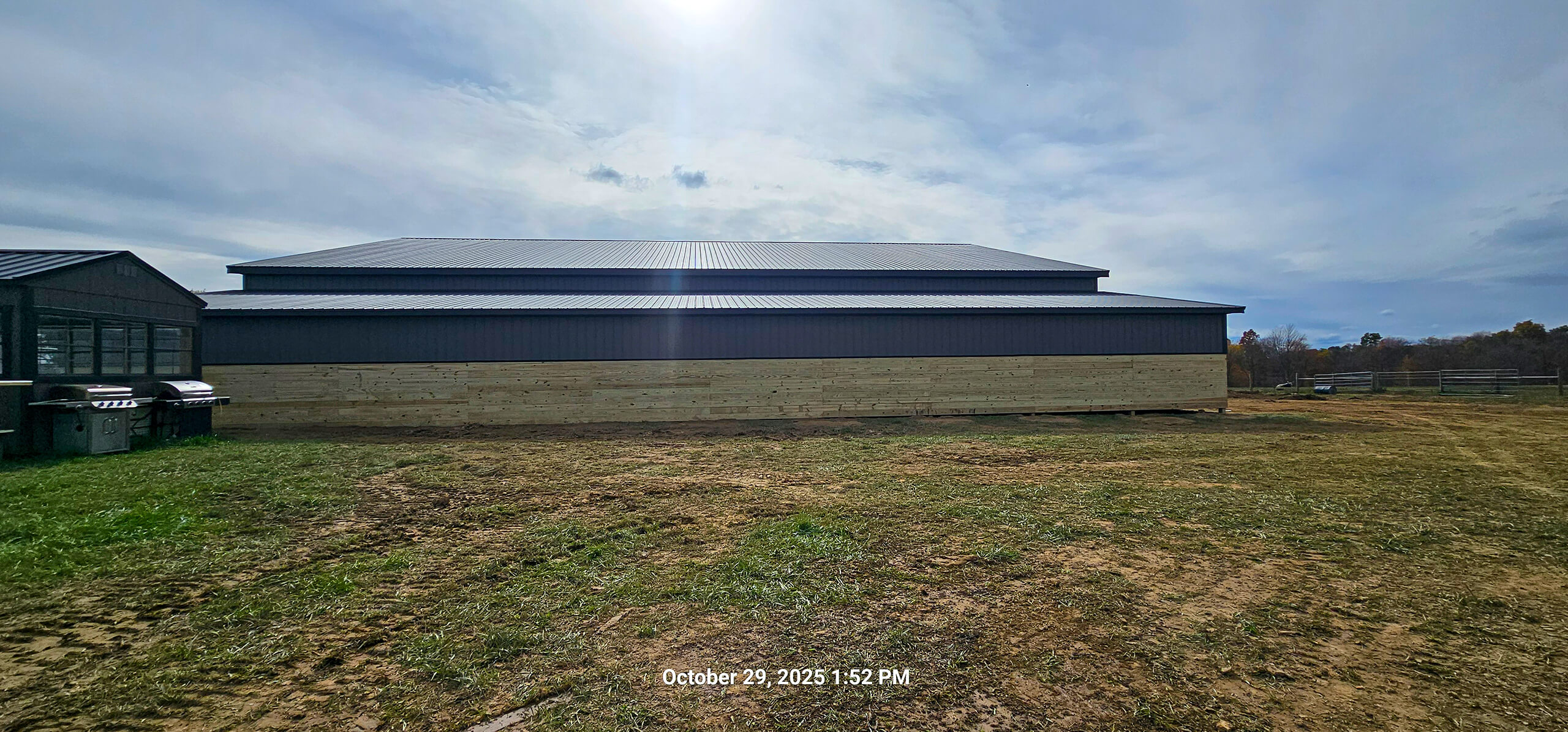 Nelson Weaver Metal Roofing Carrollton OH A large barn-like building with a metal roof and wooden lower siding sits on a patchy grassy area under a cloudy sky.