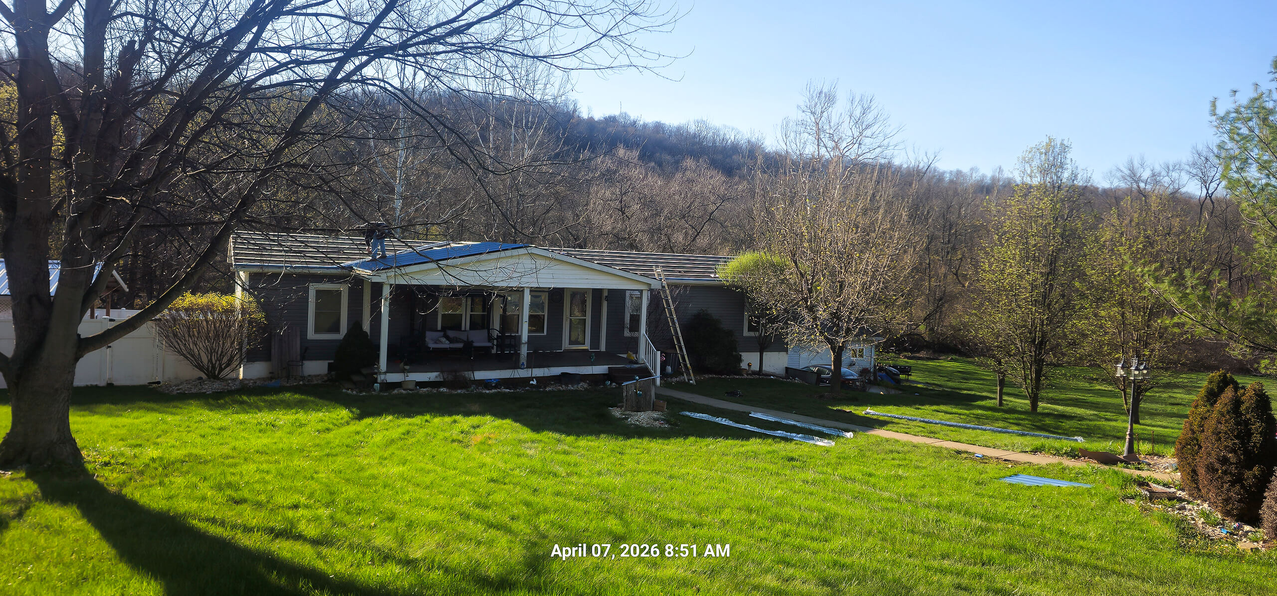Nelson Weaver Metal Roofing Carrollton OH A single-story house with a covered porch sits on a grassy lawn with trees and hills in the background. The timestamp reads April 07, 2026, 8:51 AM.