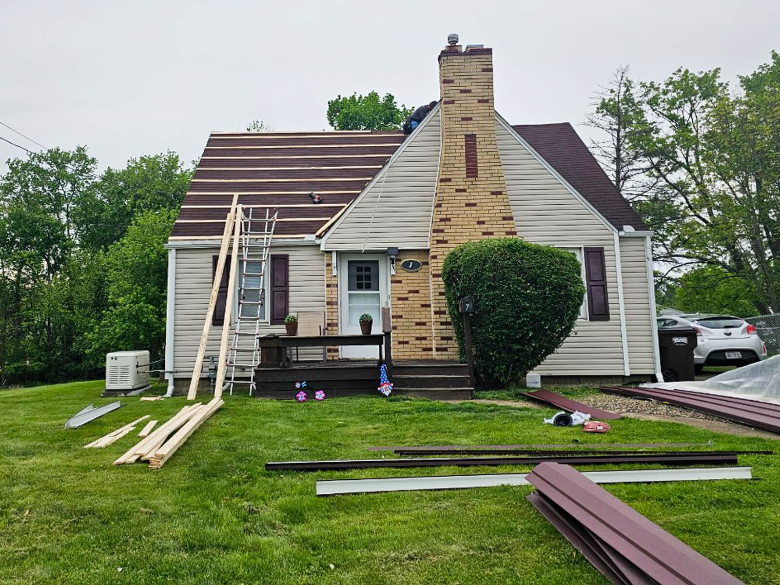 Nelson Weaver Metal Roofing Carrollton OH A house with a partially completed new roof, construction materials and ladders on the lawn, and two cars parked beside the house.