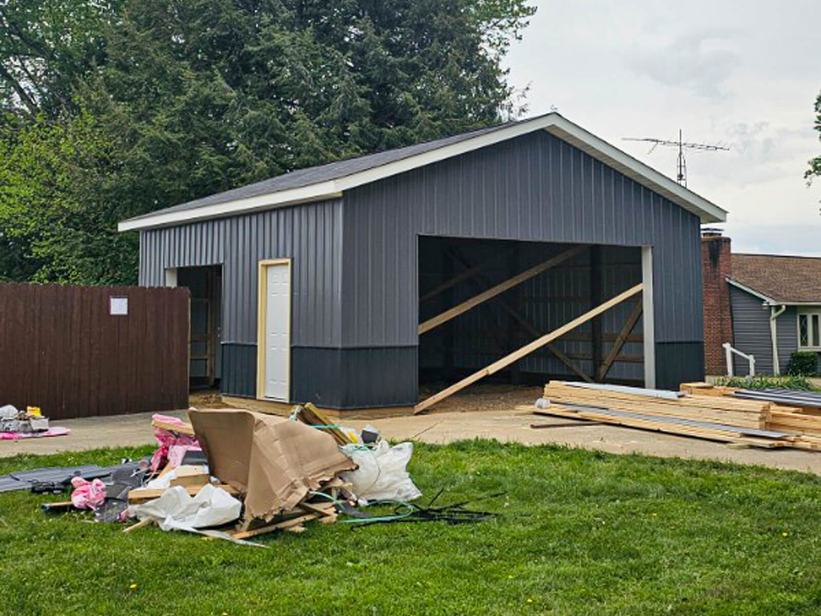 Nelson Weaver Metal Roofing Carrollton OH A partially constructed gray garage with support beams, scattered construction materials, and debris visible in the yard.