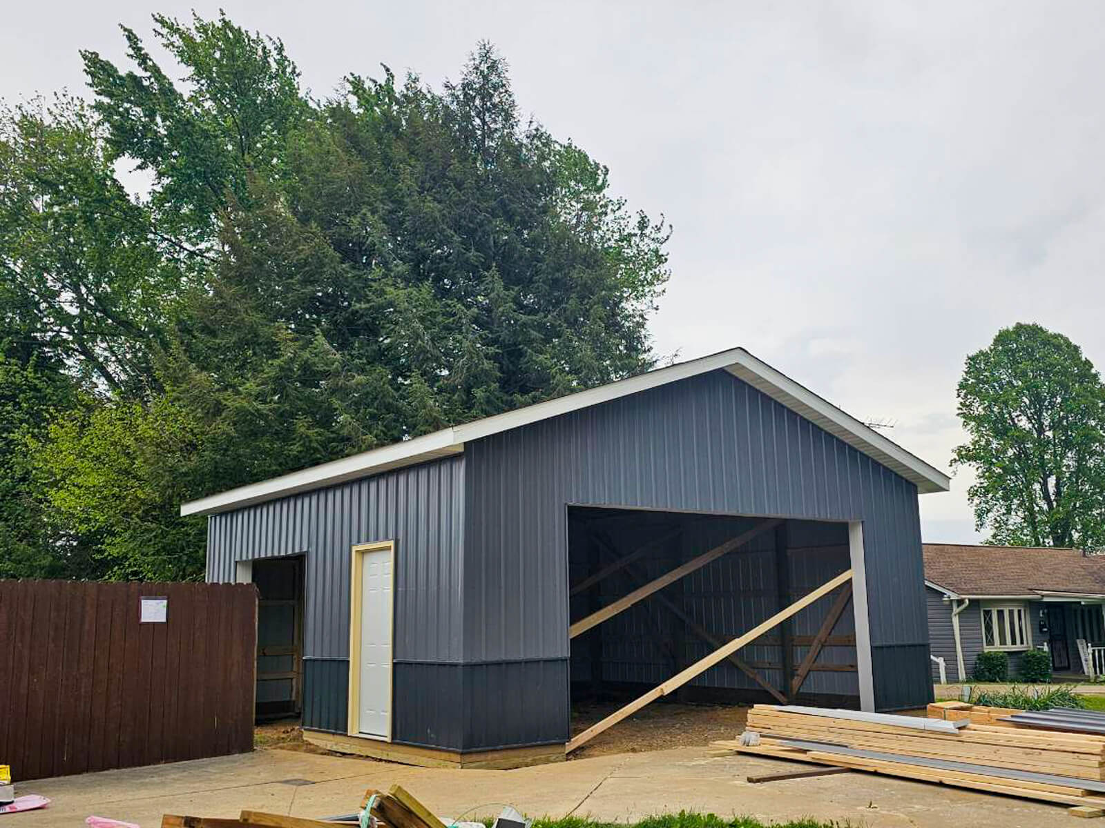 Nelson Weaver Metal Roofing Carrollton OH A partially constructed gray metal garage with open front, wooden supports, and building materials scattered on the ground nearby.