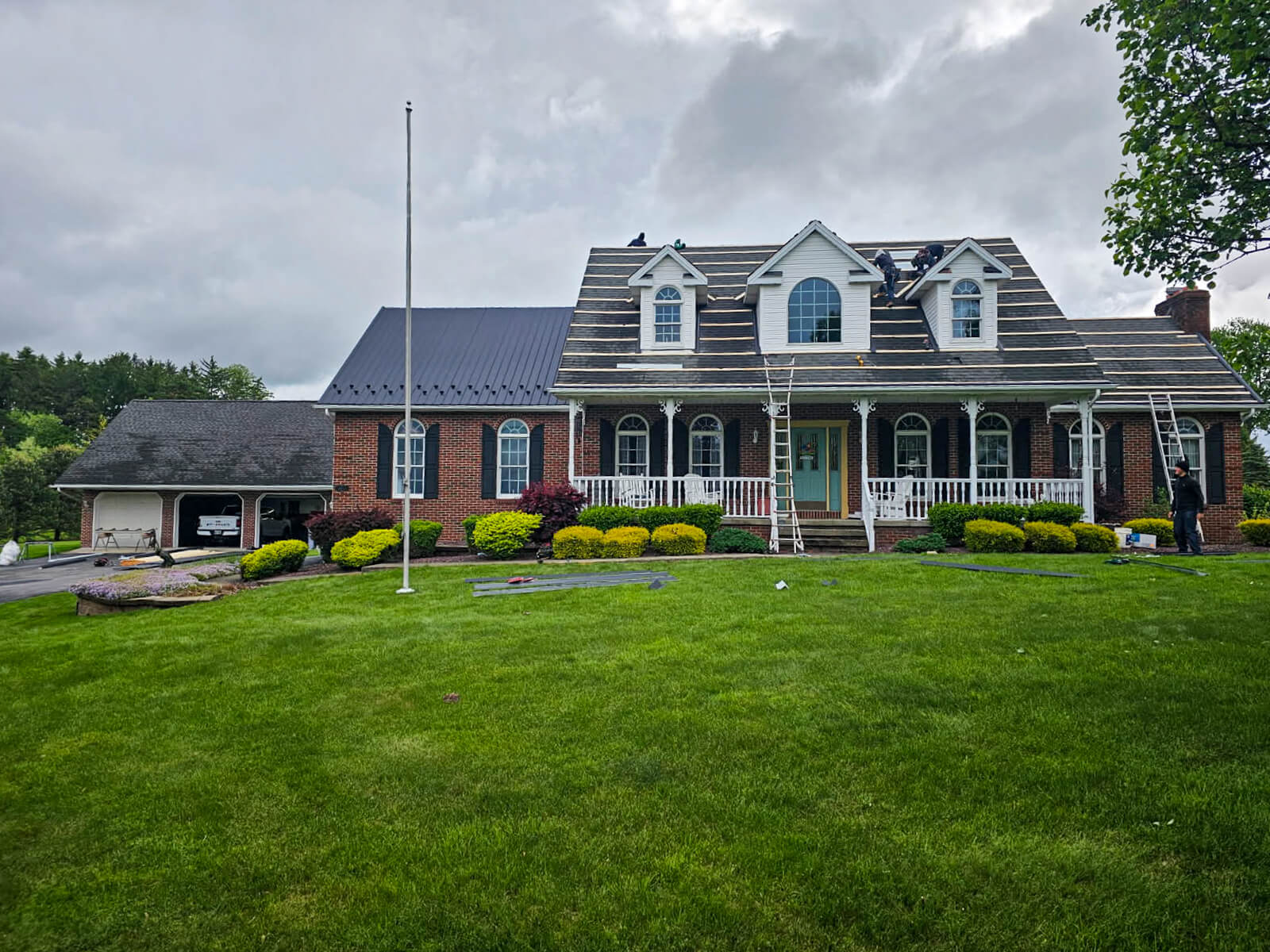 Nelson Weaver Metal Roofing Carrollton OH A two-story brick and siding house with dormer windows, a covered front porch, and scaffolding set up on the roof; garage on the left, green lawn in front.