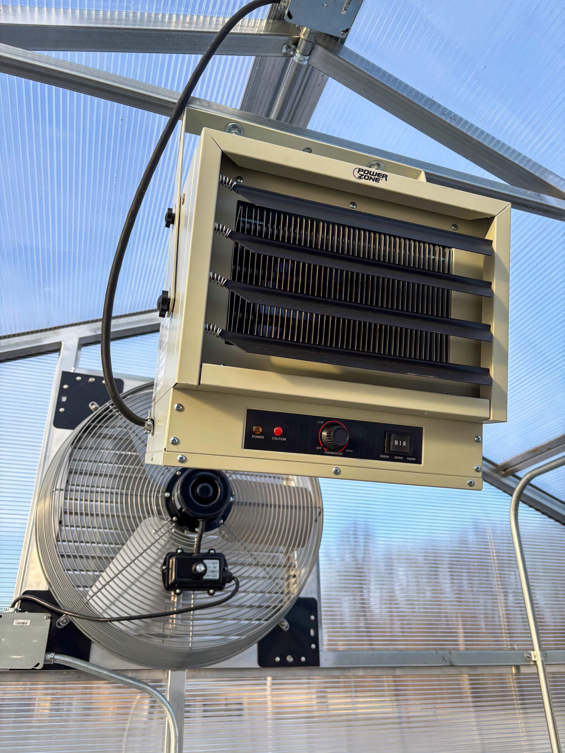 Sunny Crest Acres Versailles MO Ceiling-mounted electric heater and large metal fan installed in a greenhouse with transparent walls and roof.