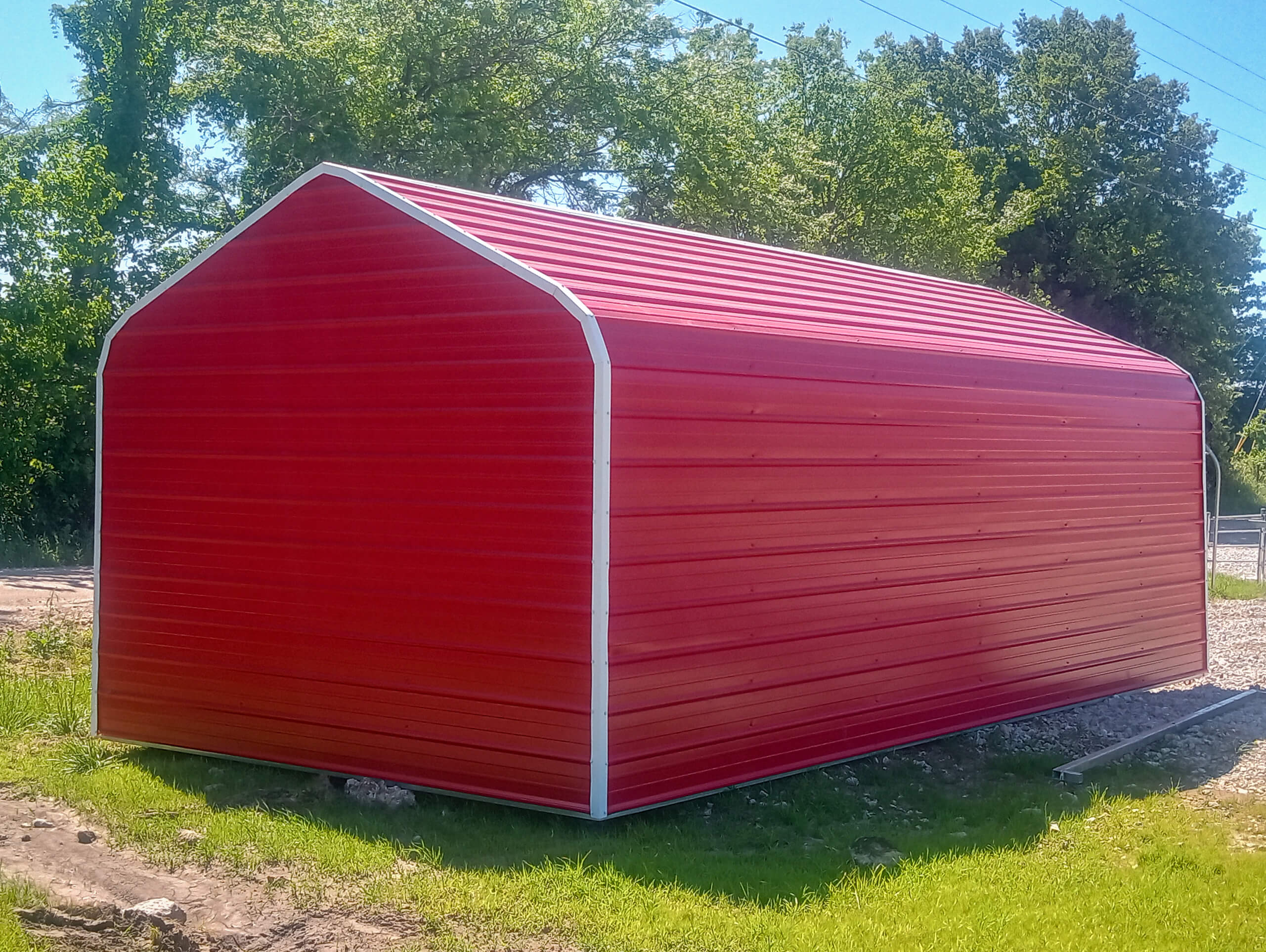 Sunny Crest Acres Versailles MO A red metal storage shed with a white trim sits on a grassy area, with trees and clear sky in the background.