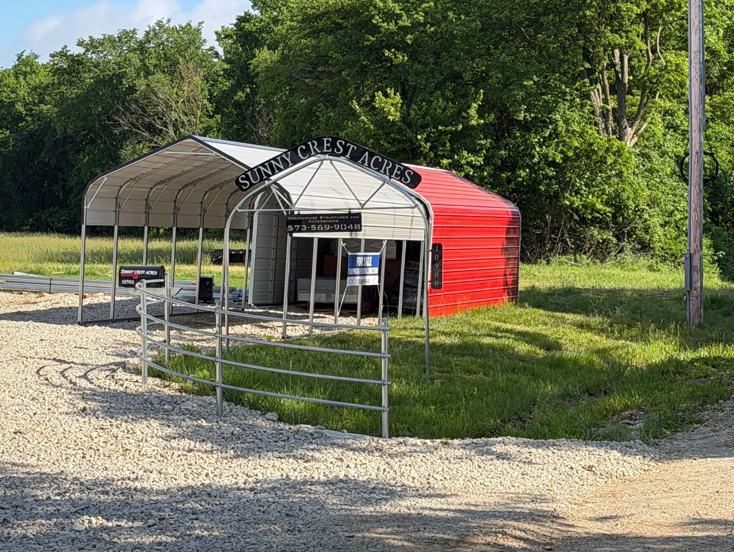 Sunny Crest Acres Versailles MO A red and gray metal building with a curved roof sits by a gravel path under a sign reading "Sunny Crest Acres." Trees and grass are in the background.