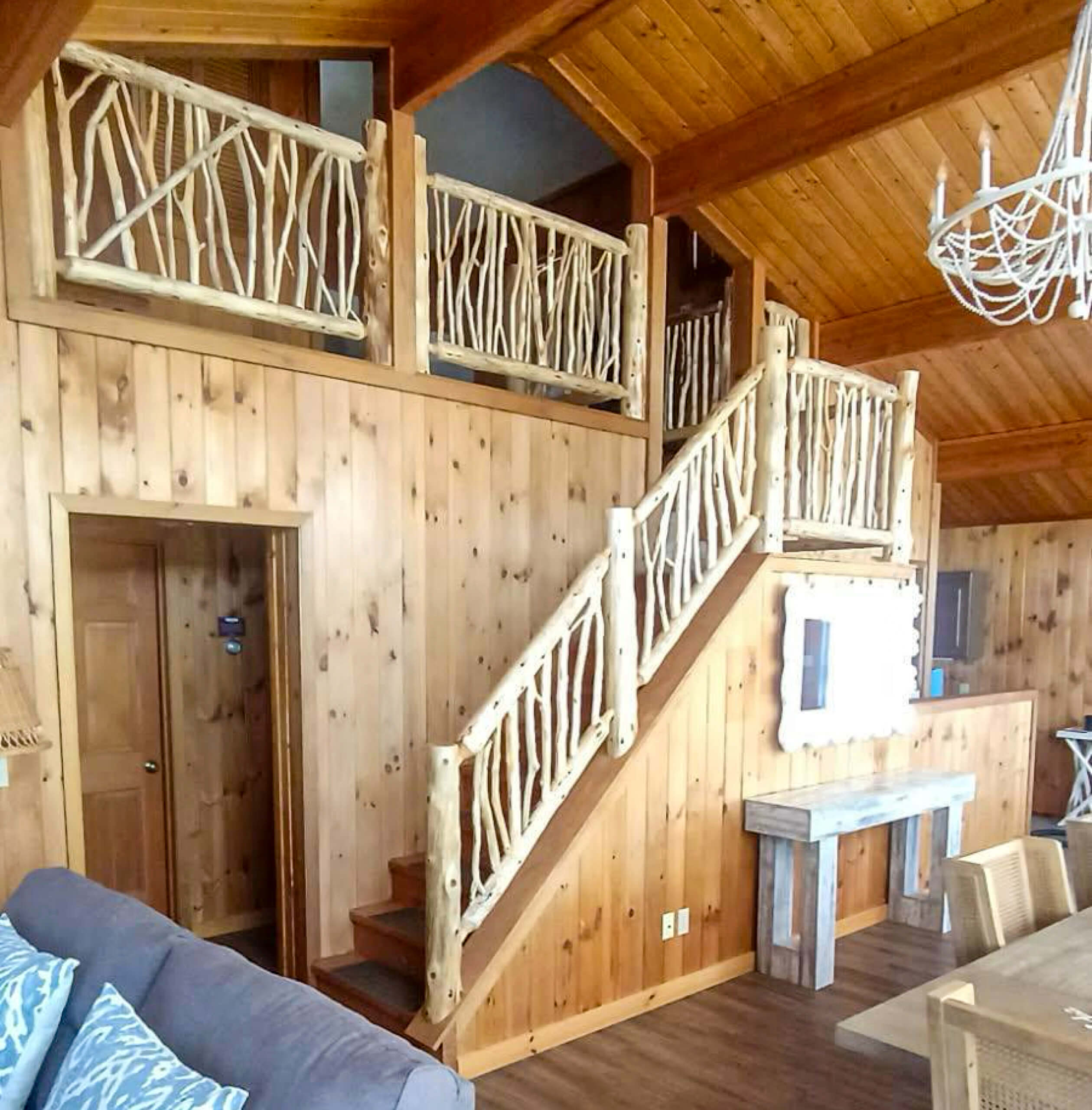 Brookview Builders Penn Yan, NY Interior of a rustic cabin featuring wood-paneled walls, a staircase with natural branch railings, and a loft area above.