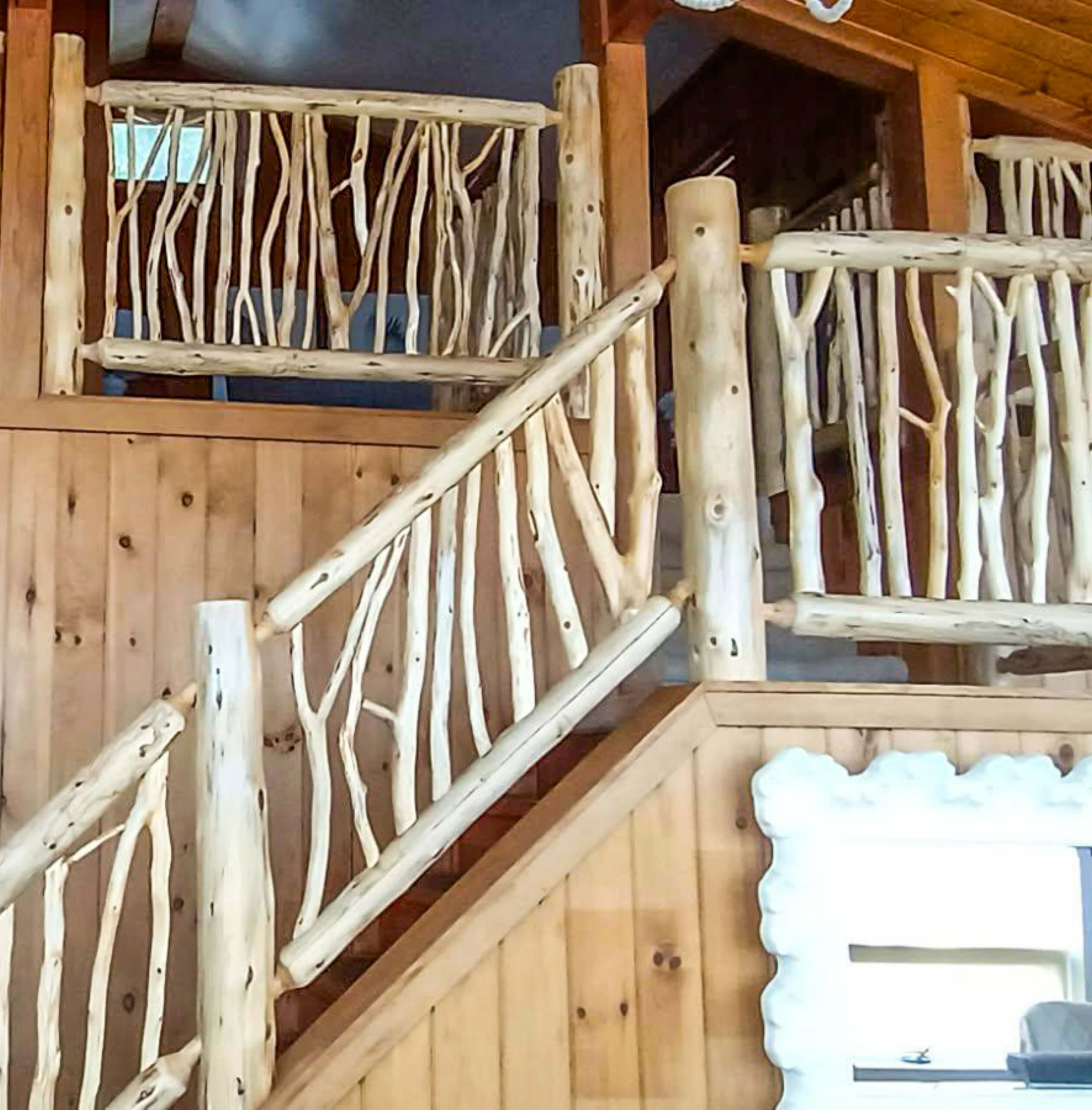 Brookview Builders Penn Yan, NY A wooden staircase with rustic railings made from natural, unfinished branches and logs is shown inside a log cabin-style interior.